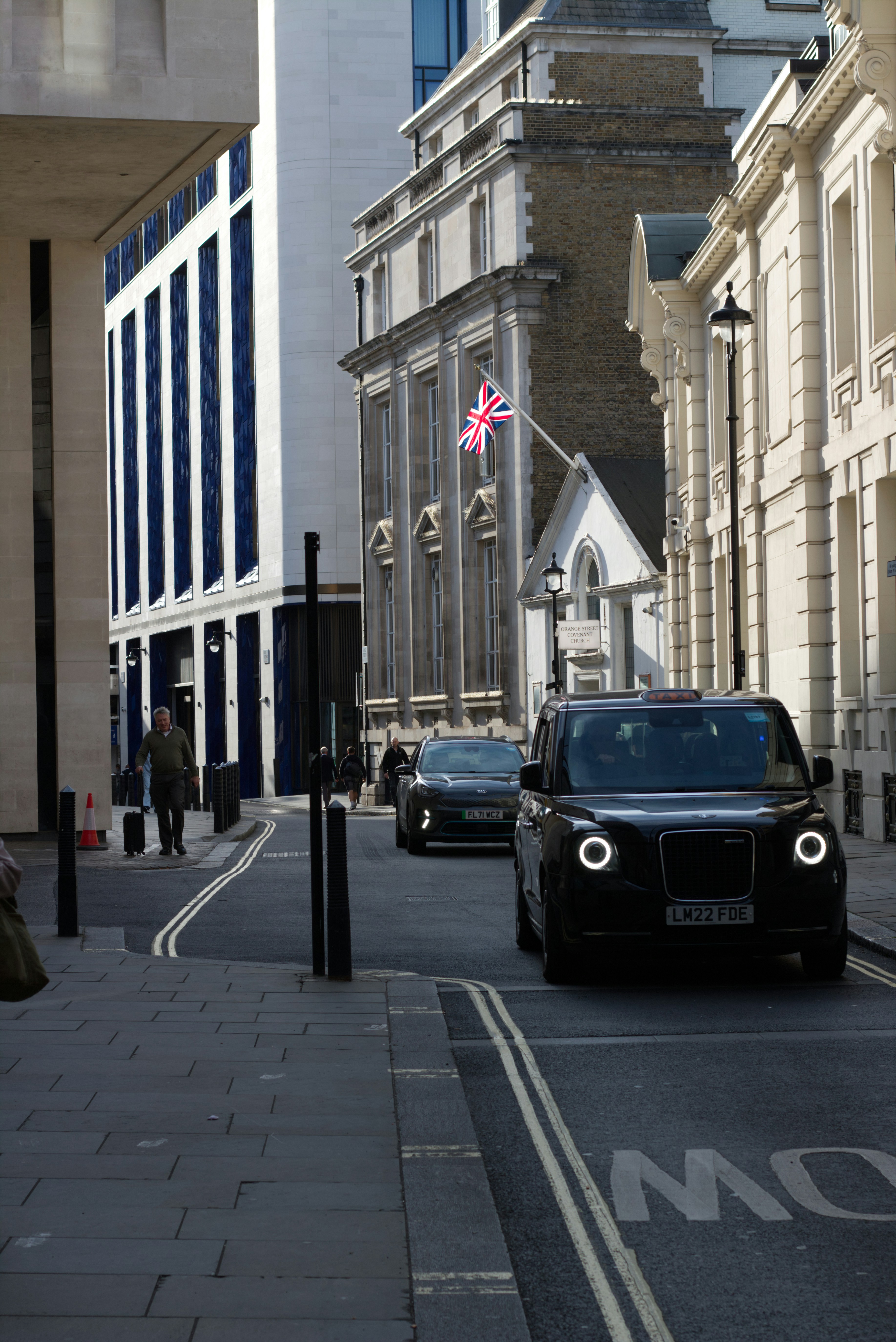 Black london taxi drives down a narrow street.