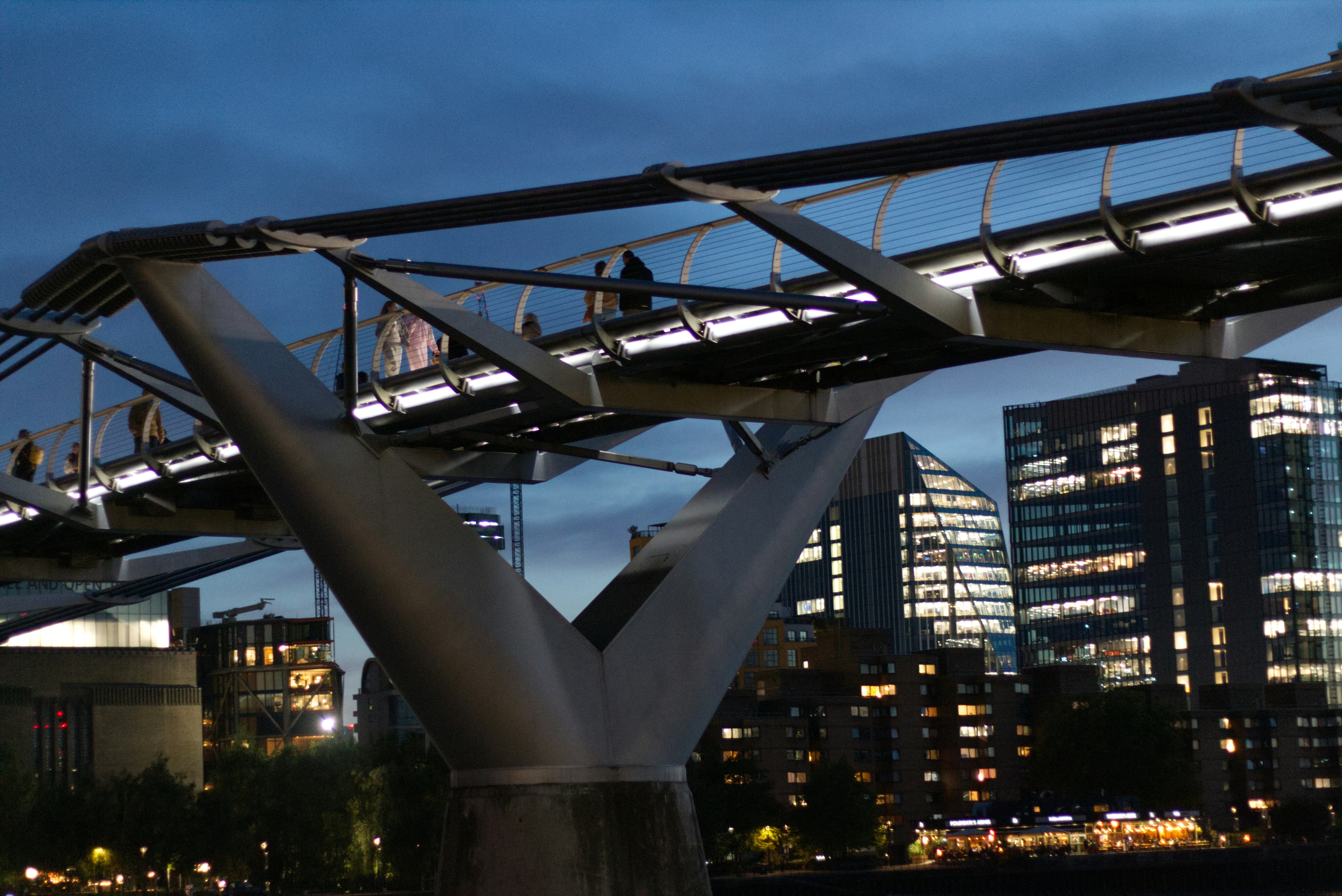 People walk across a modern bridge at dusk.