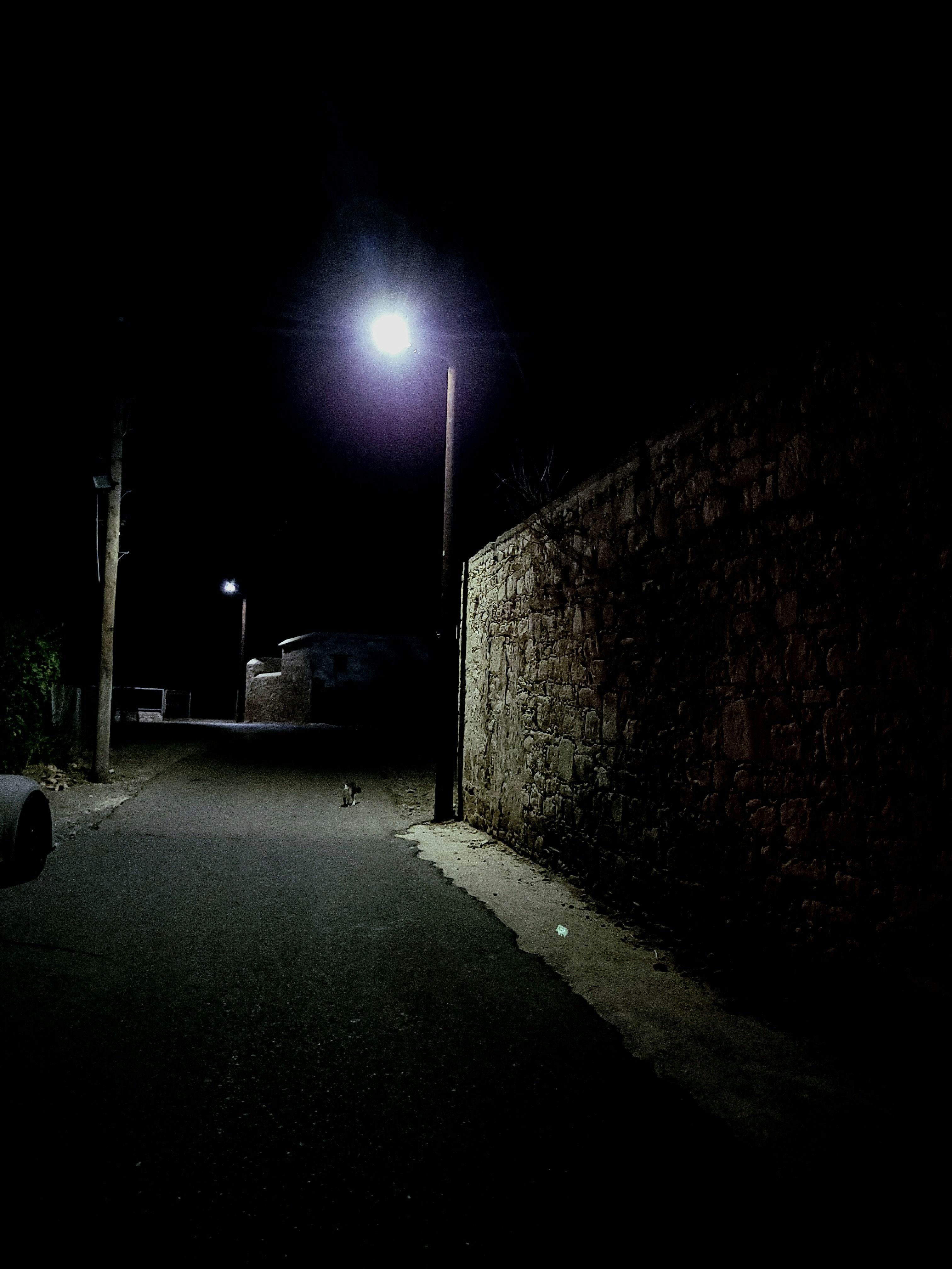 A dimly lit street at night with a stone wall.