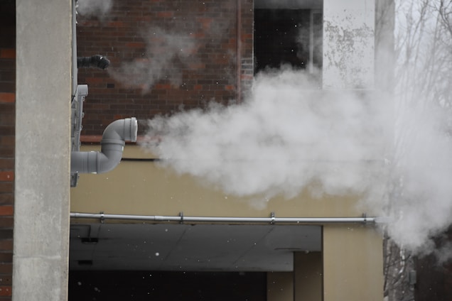 Steam billowing from a pipe on a brick building.