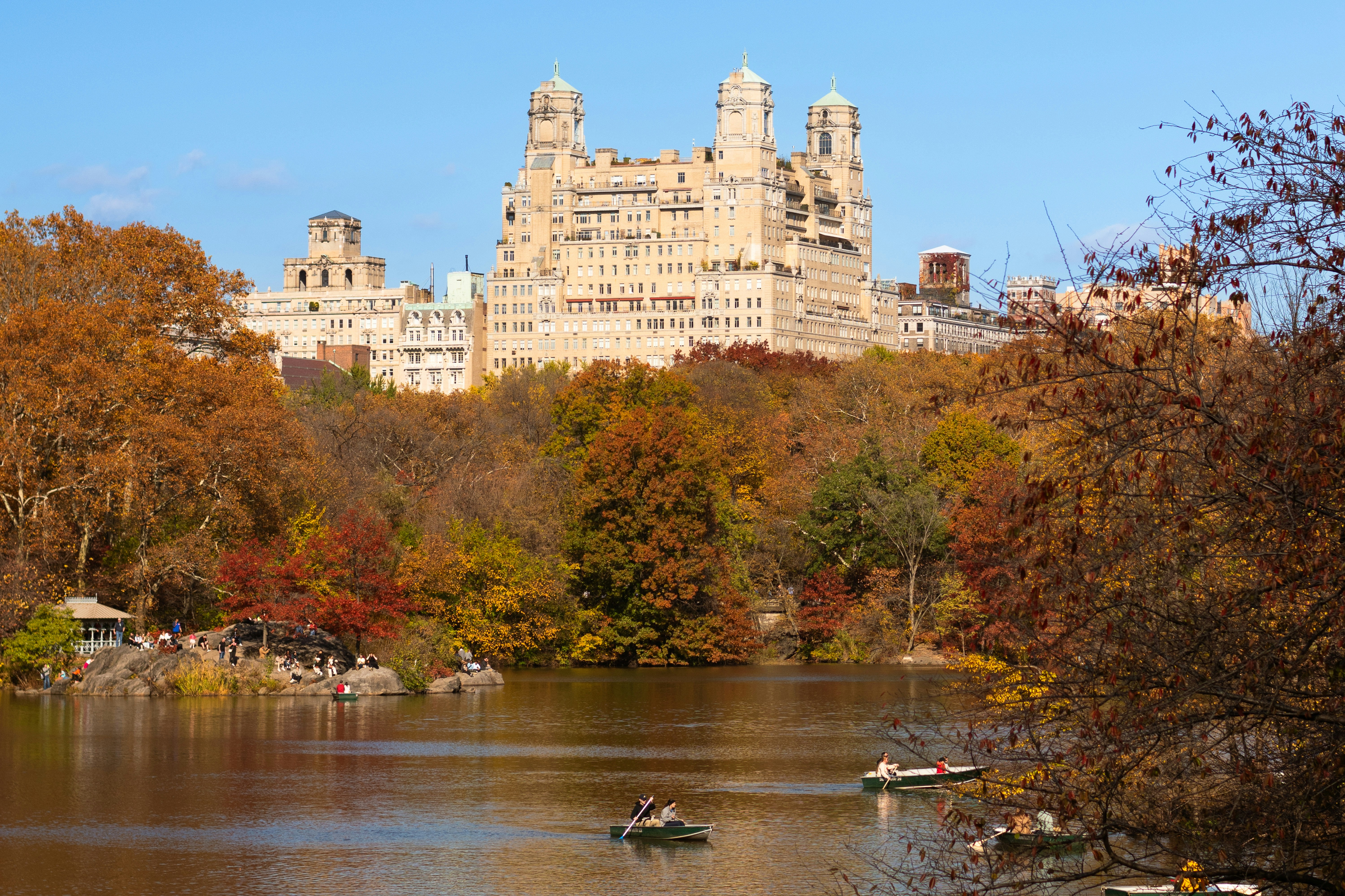 Autumn trees surround a lake with boats and buildings.