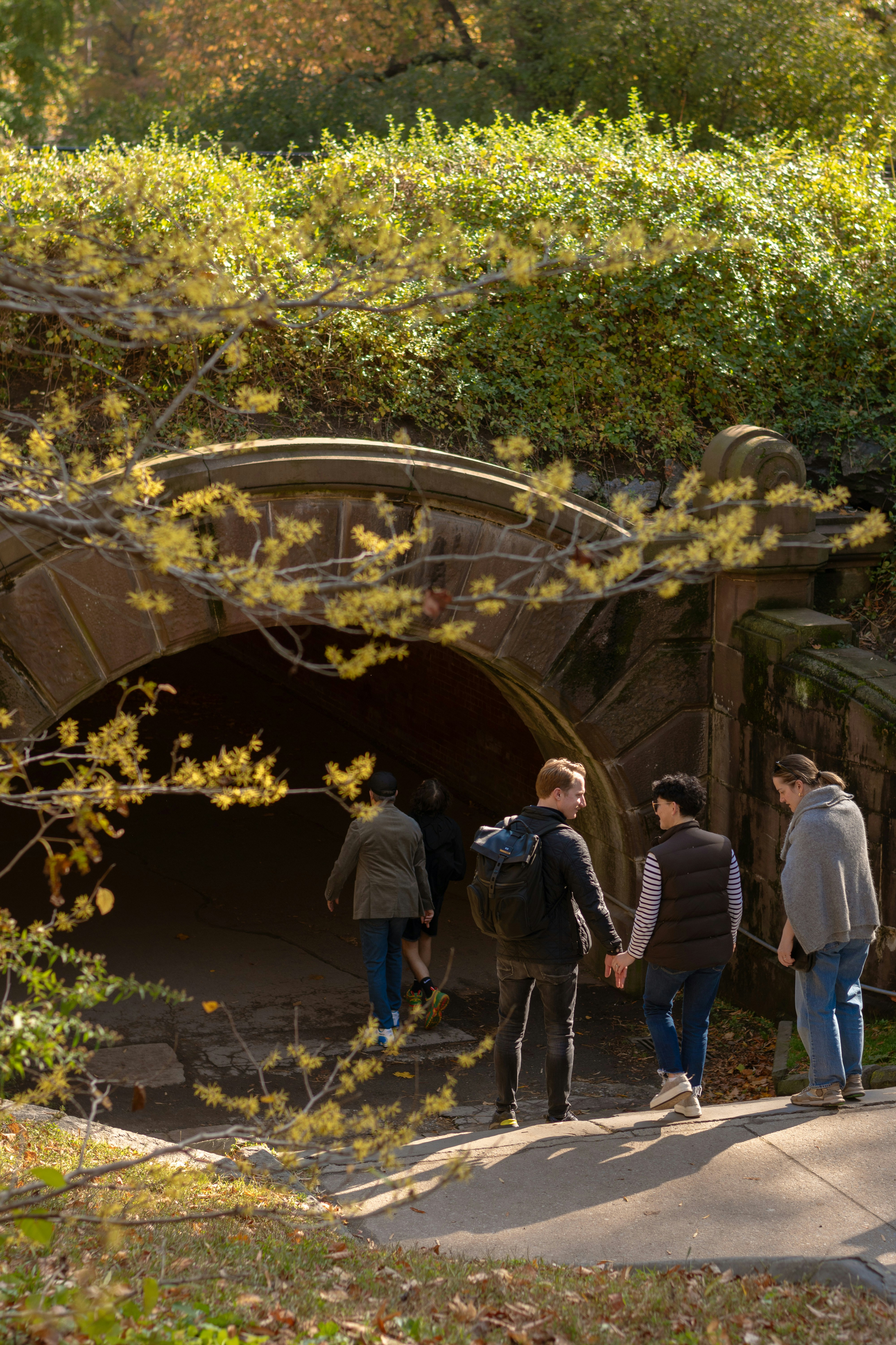 People walk towards a stone archway in a park.