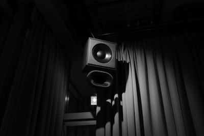 A speaker hangs in front of dark curtains.