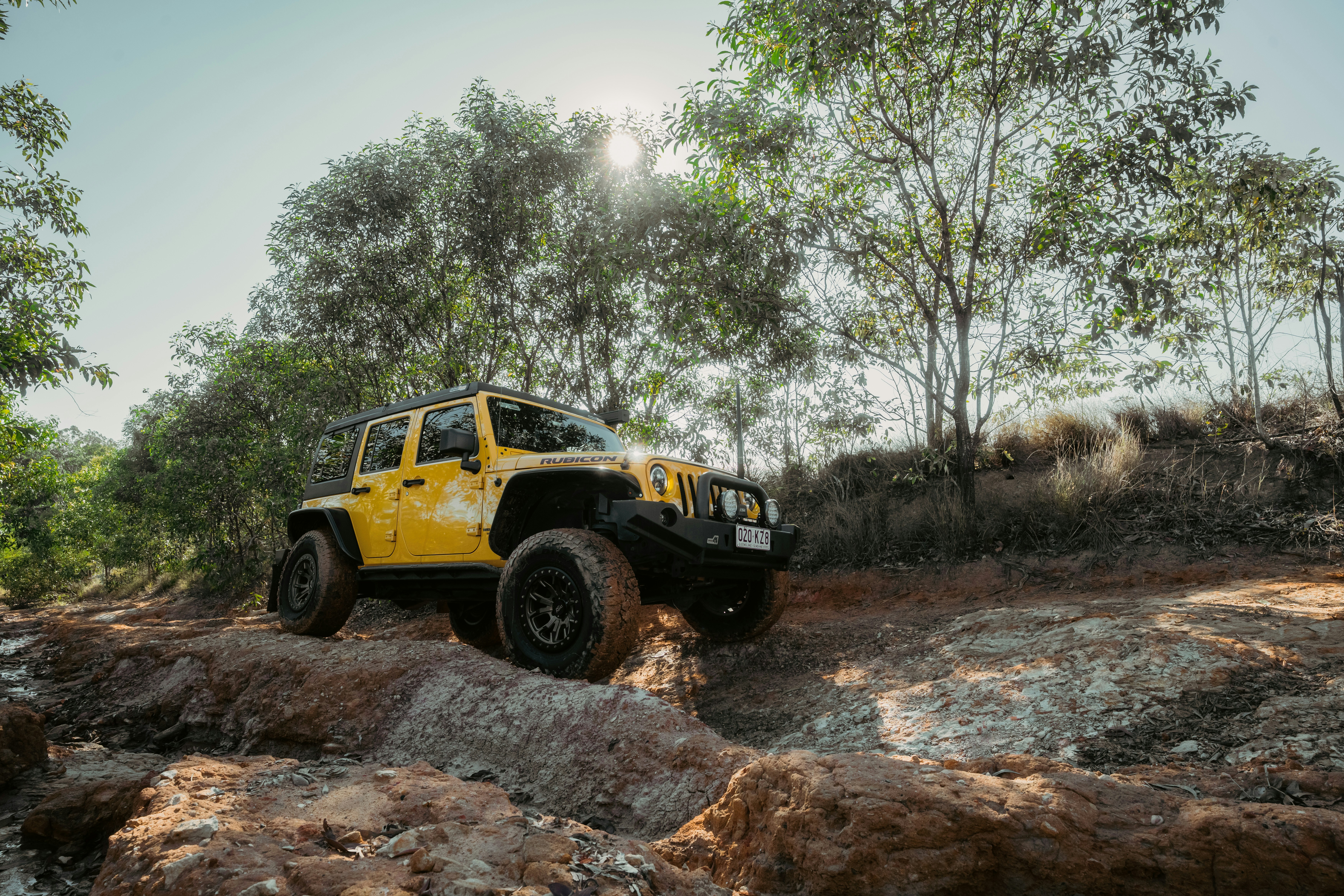 Yellow jeep driving on a rocky, wooded trail.