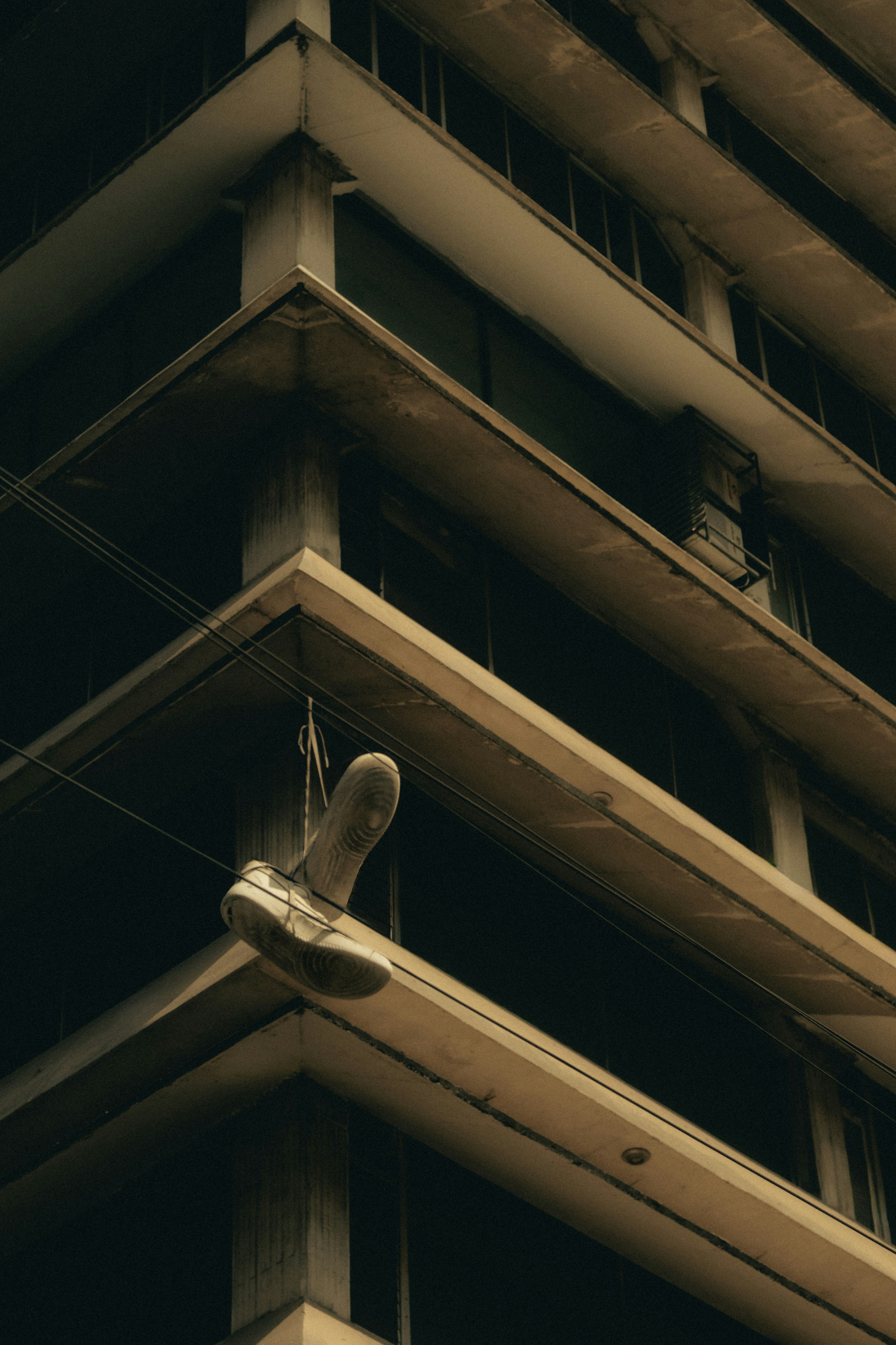 A single shoe hangs from wires on a building.