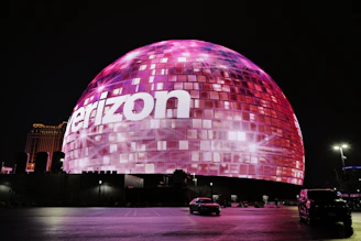 A glowing spherical building with the verizon logo at night.