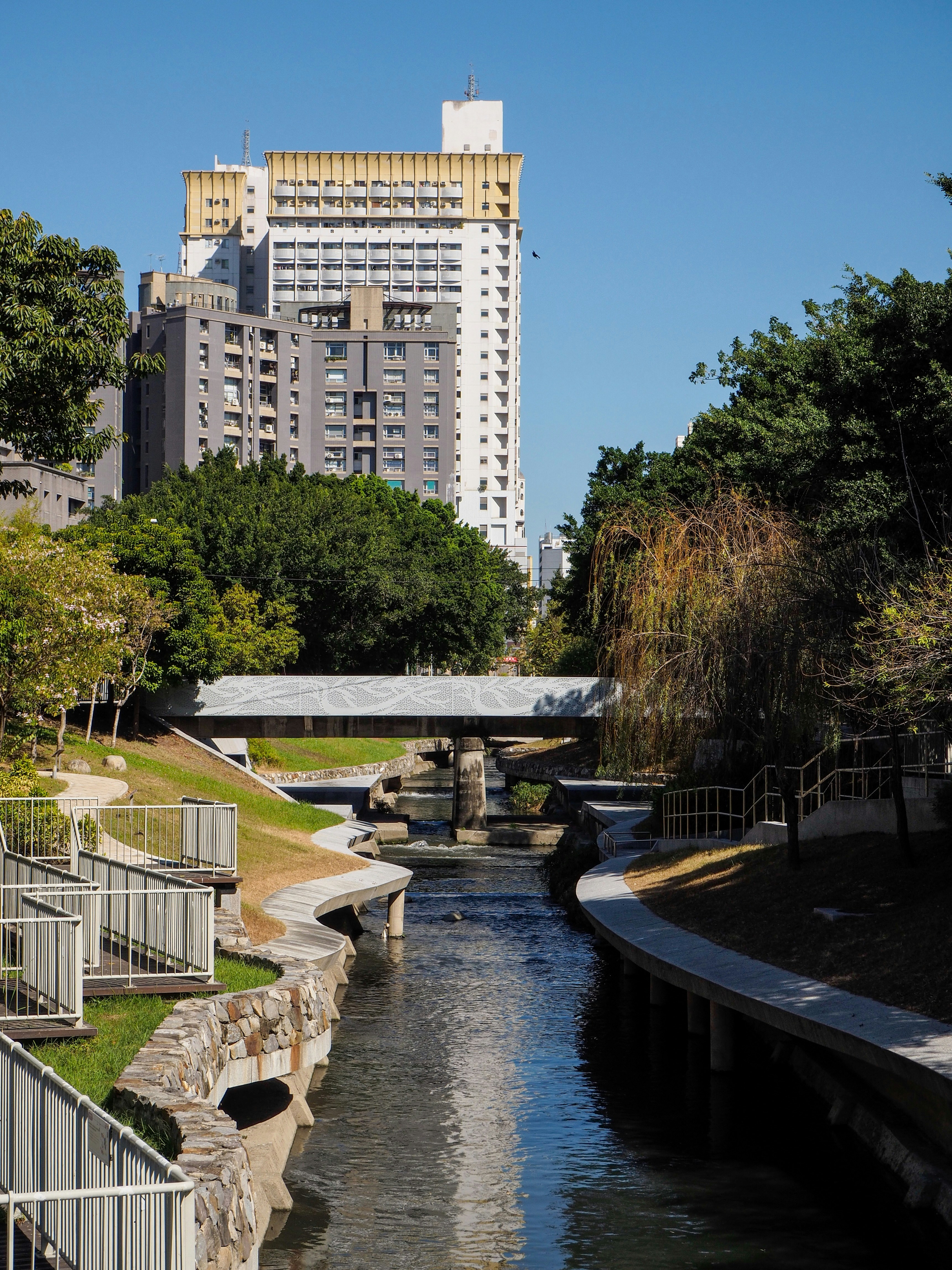 River flowing through a park with buildings beyond.