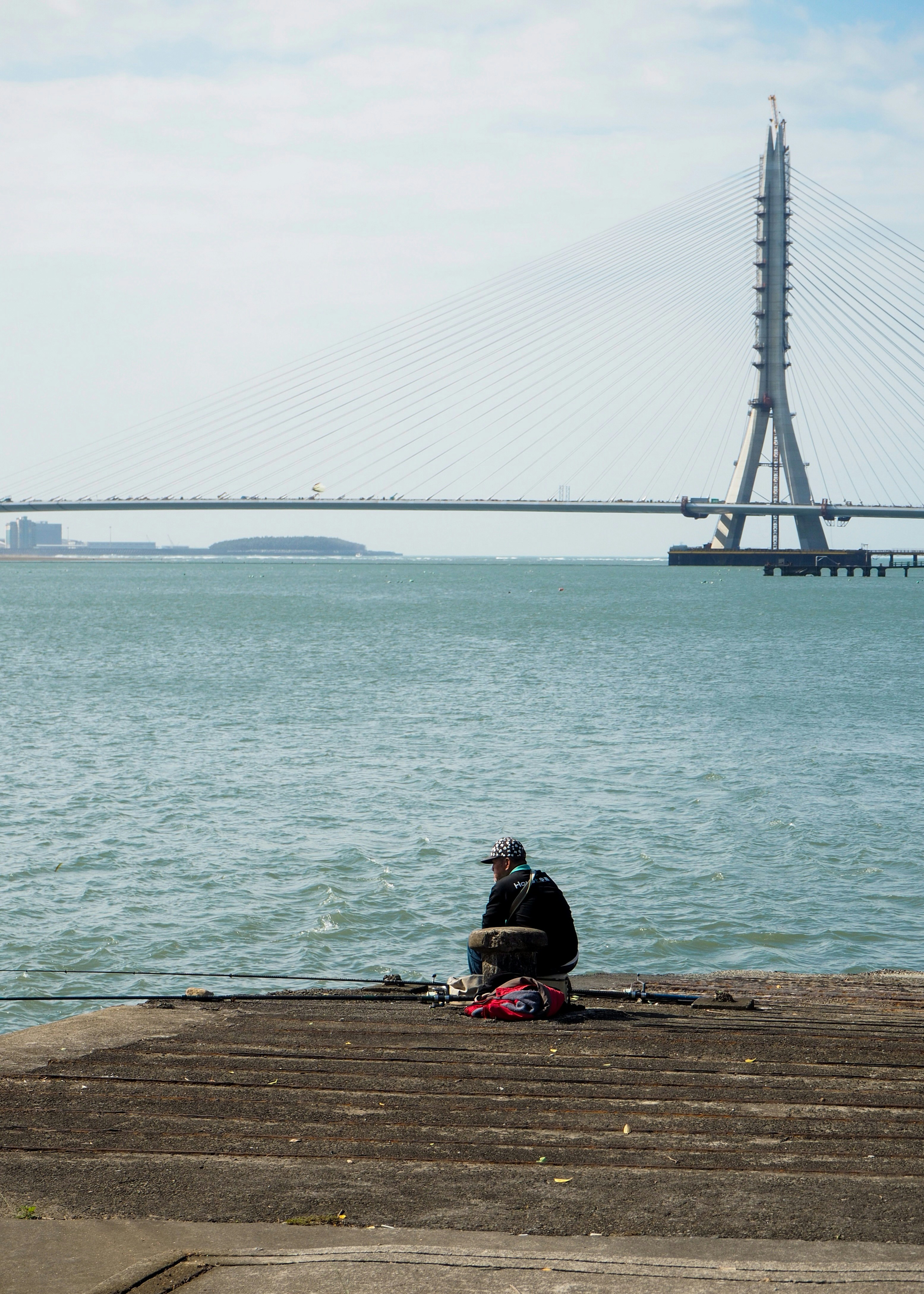 Fisherman sitting by the water with a bridge behind him