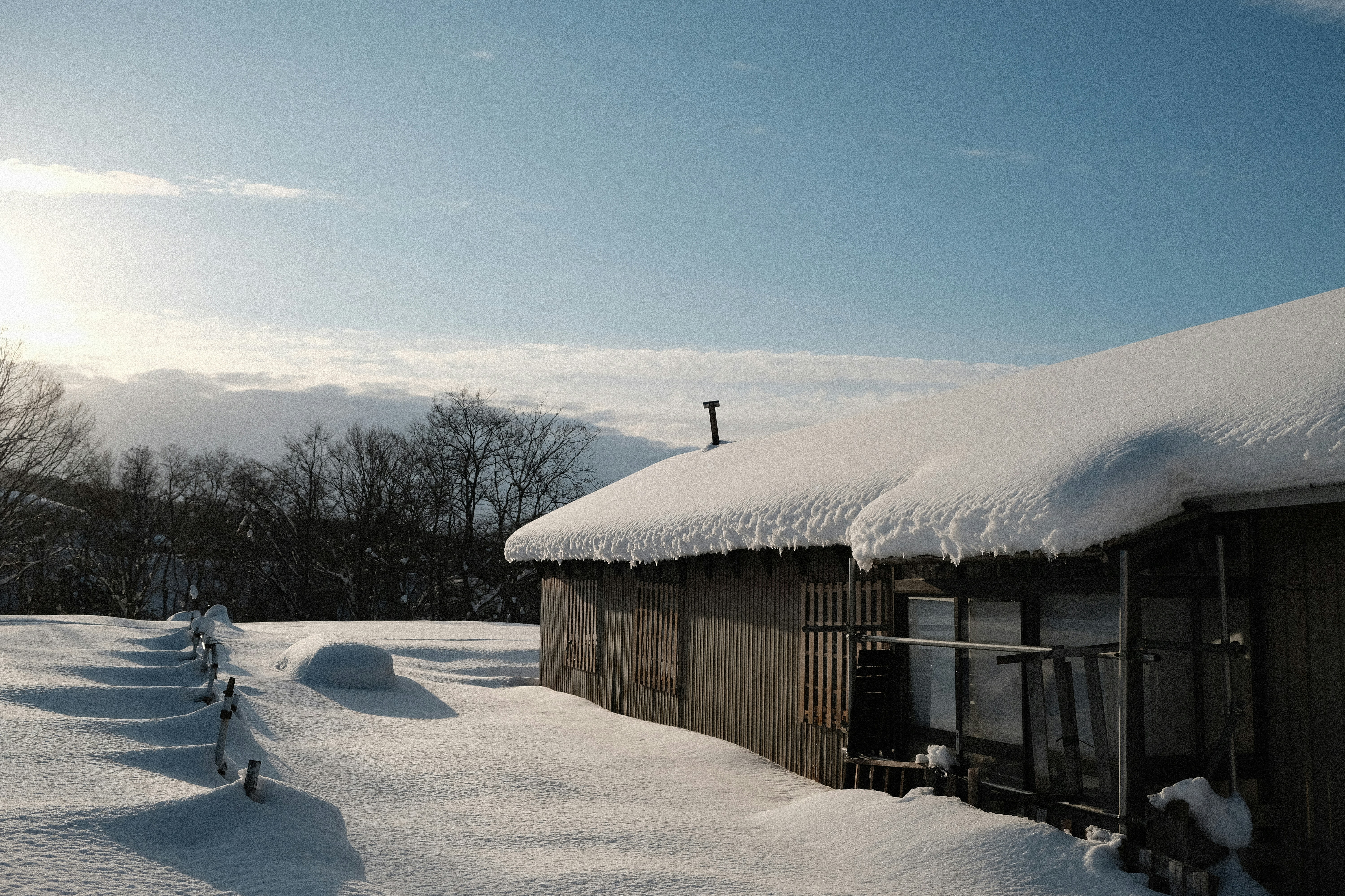 A wooden building covered in snow under a blue sky.