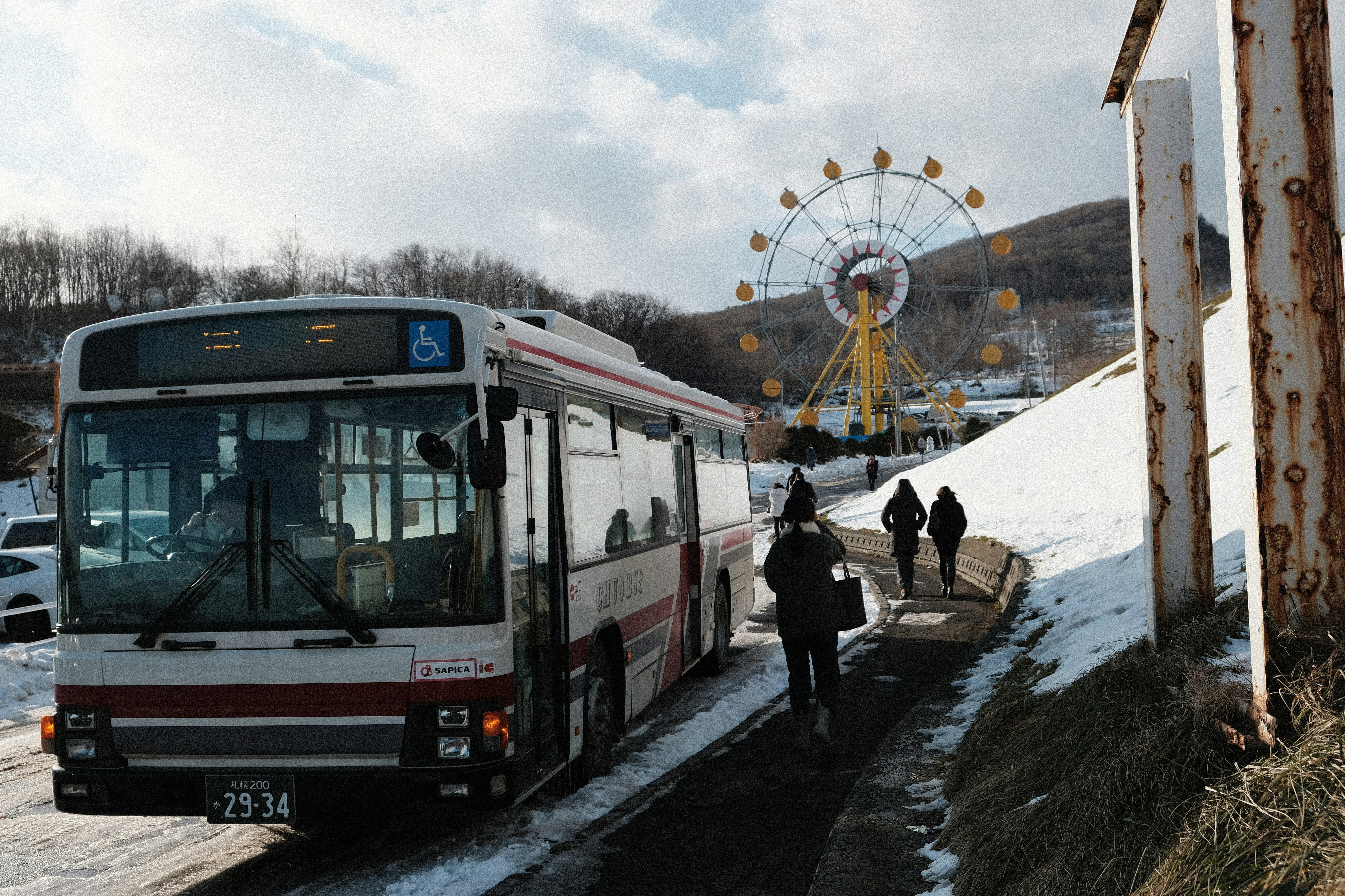 Bus waits by snowy path with ferris wheel