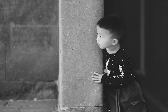 A young boy peeking around a stone pillar.
