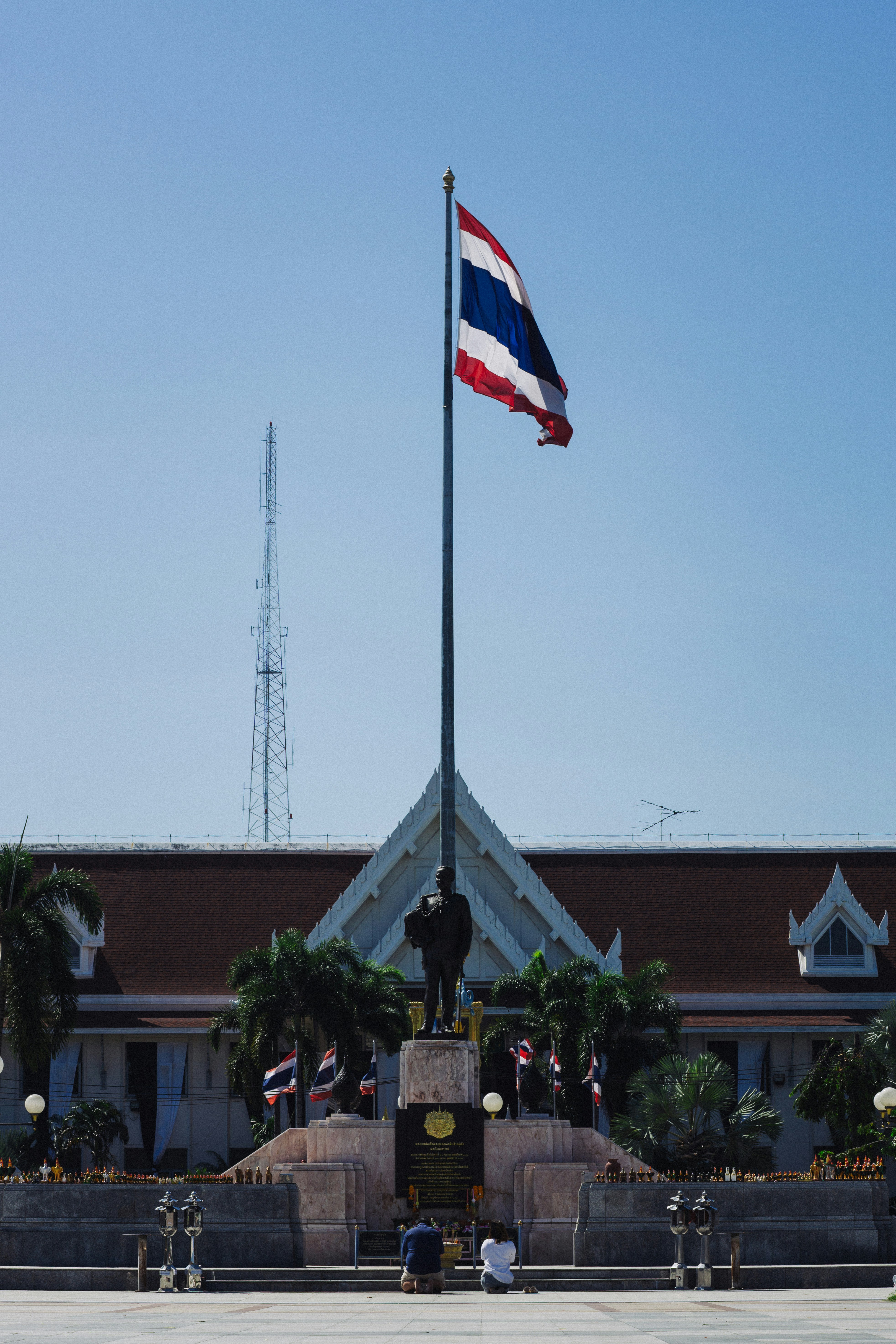 Thai flag flies over monument with people kneeling