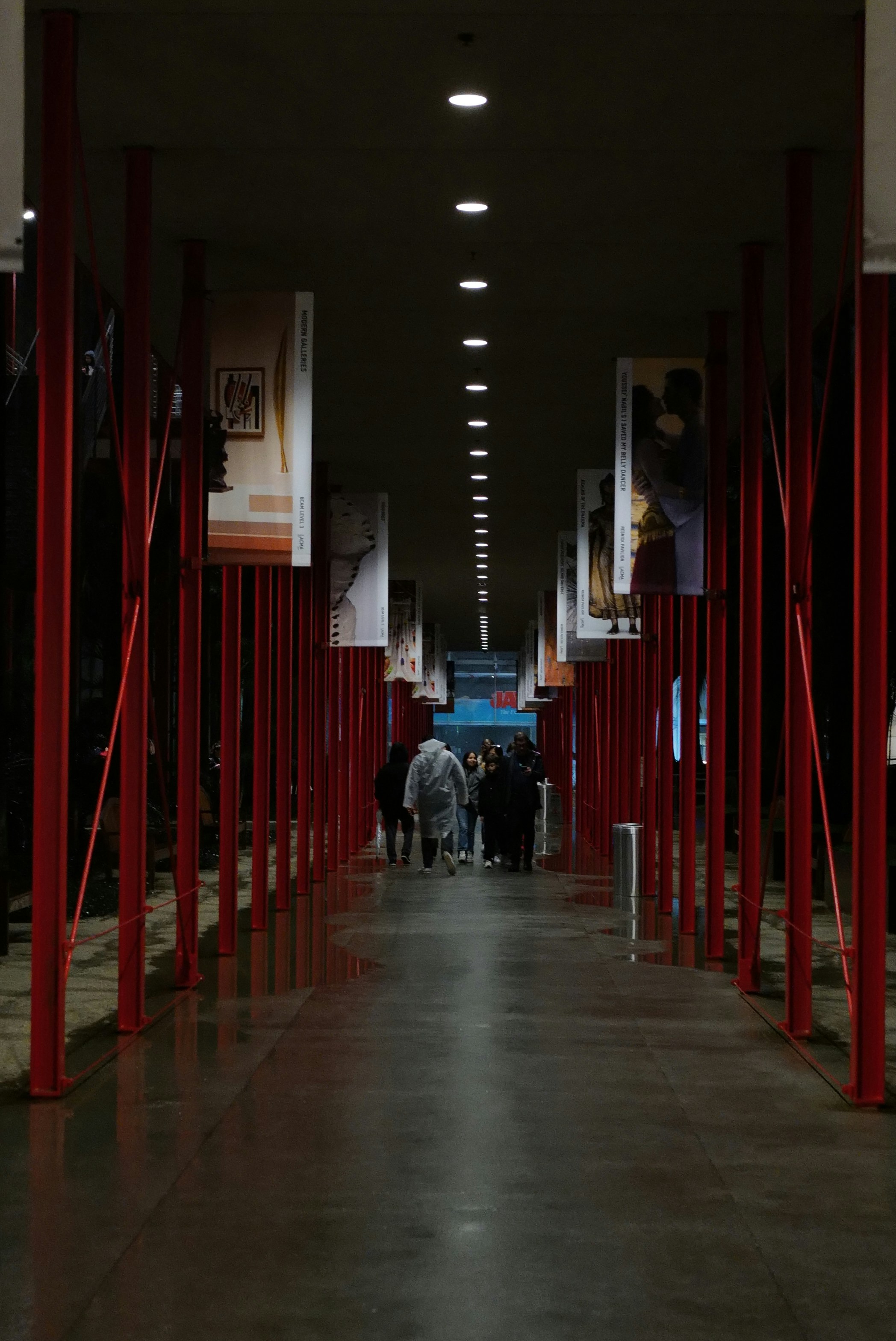 People walking down a long, modern hallway with red pillars.