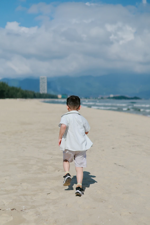 Young boy runs on a sandy beach towards the ocean.