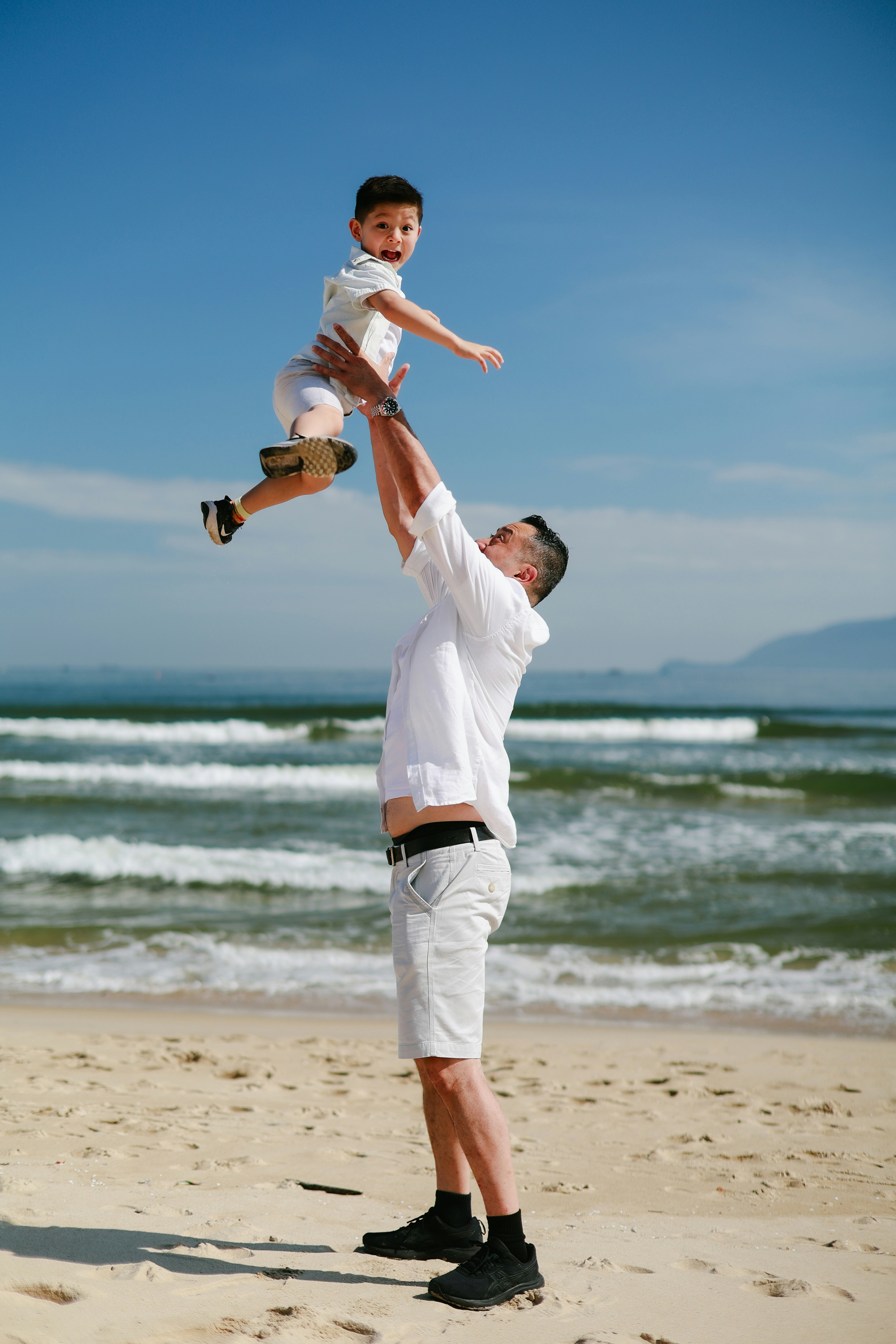 Father throws son in the air at the beach.