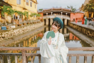 Woman in traditional dress holding a fan on a bridge.