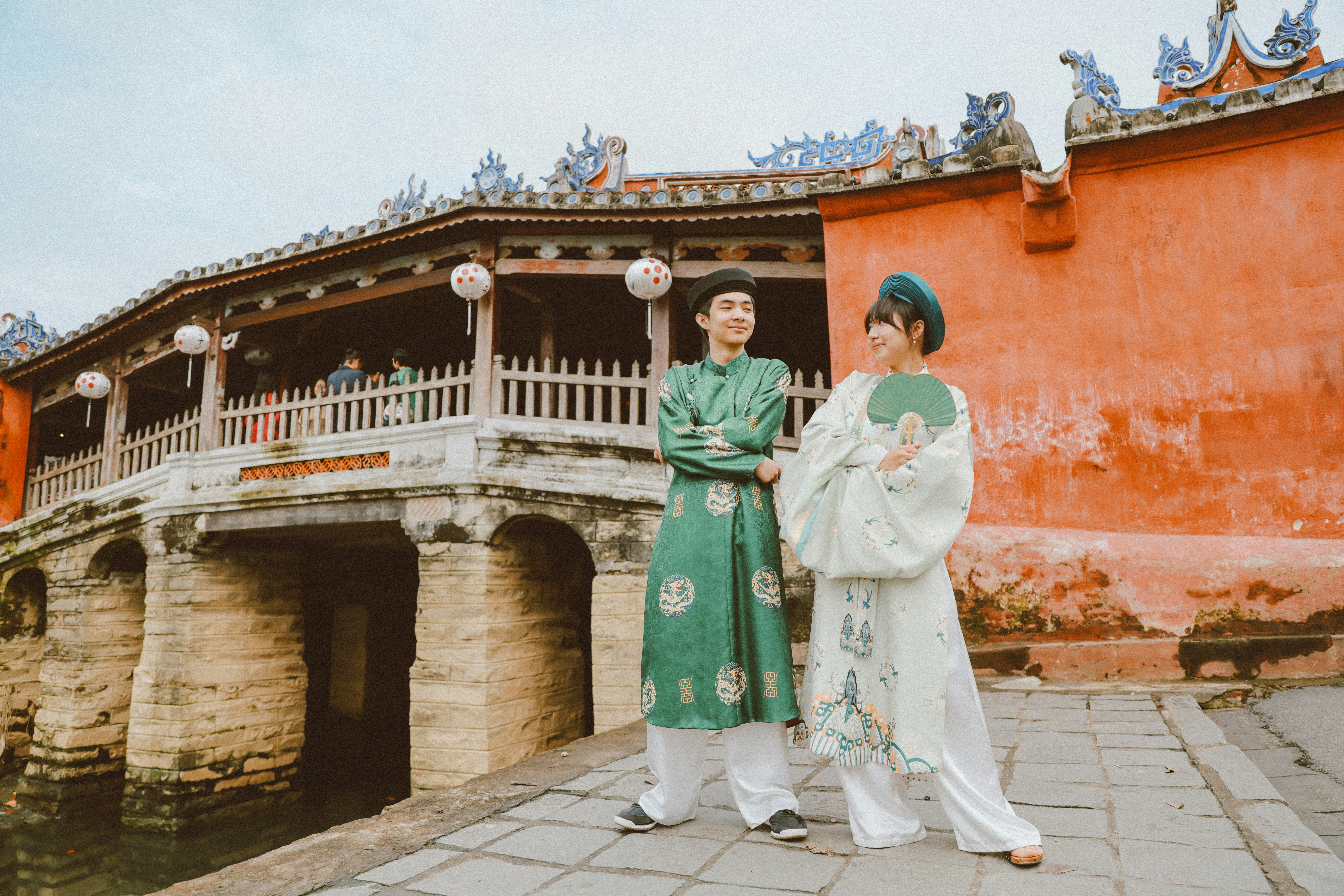 Couple in traditional vietnamese áo dài standing on bridge.