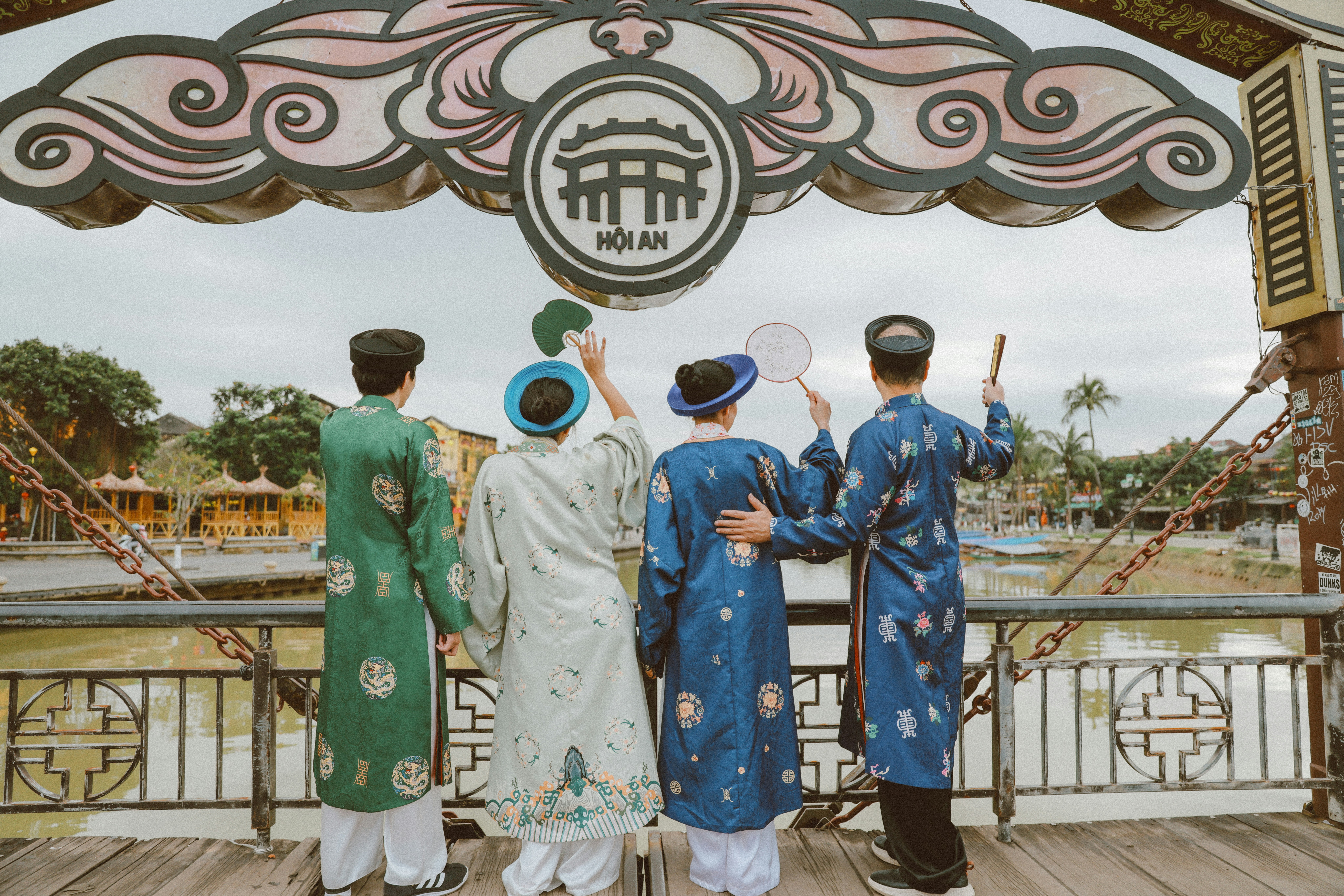 Four people in traditional vietnamese ao dai looking at bridge