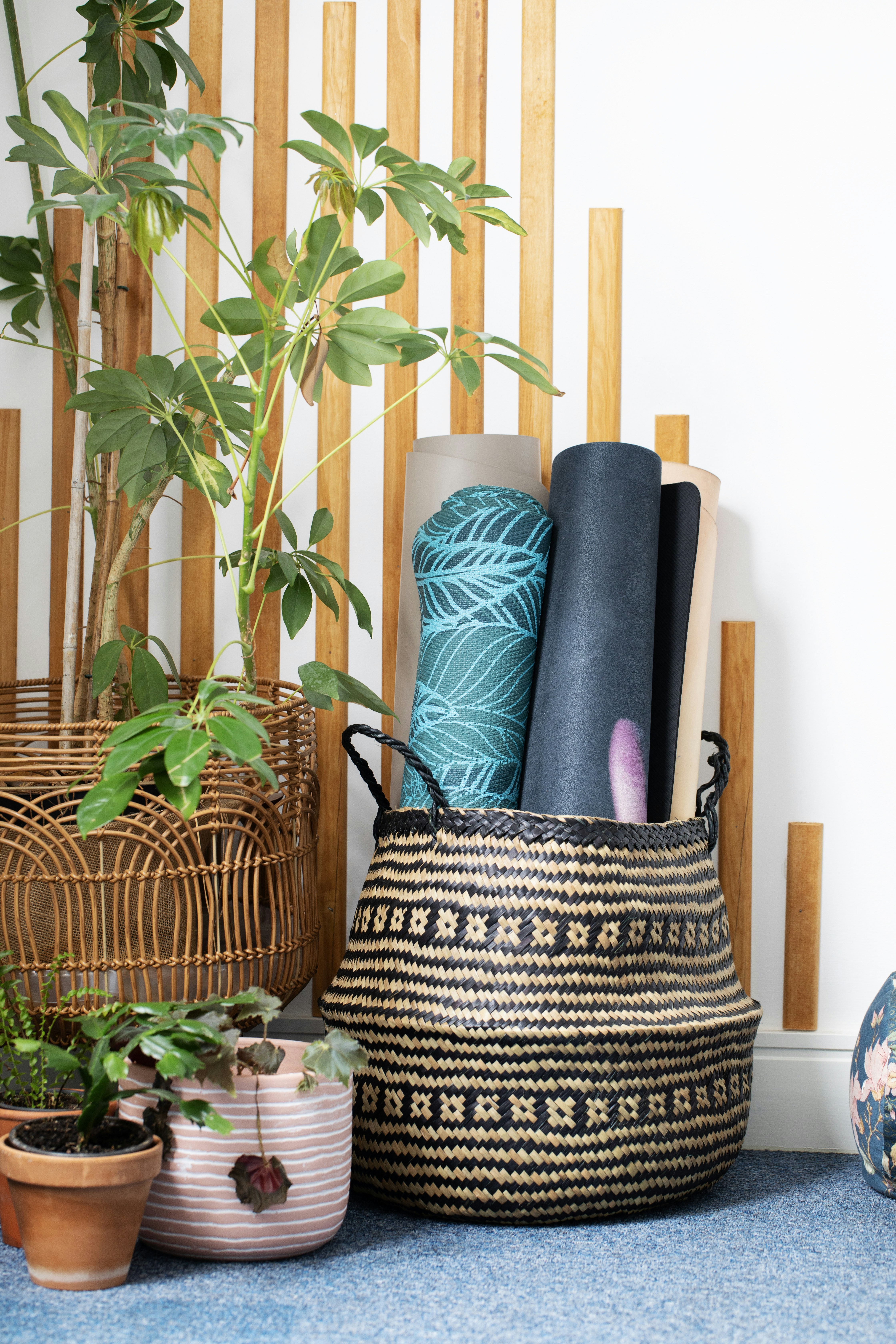 Rolled yoga mats in a decorative basket with plants.