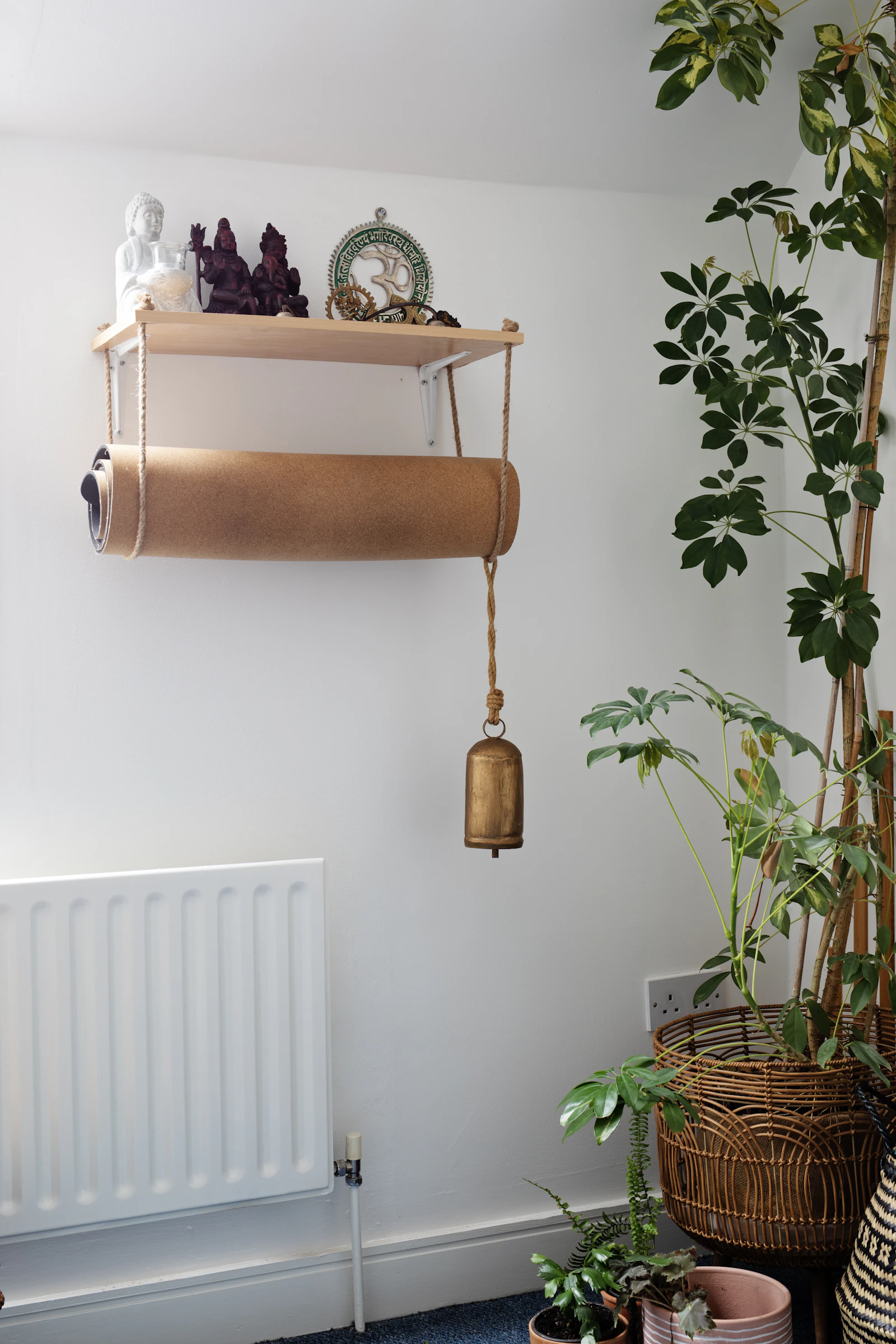 A rolled yoga mat and a small brass bell hanging on the shala wall