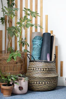 Rolled yoga mats in a woven basket with plants.