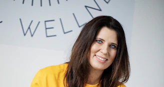 A woman with dark hair smiles in a yellow sweatshirt.