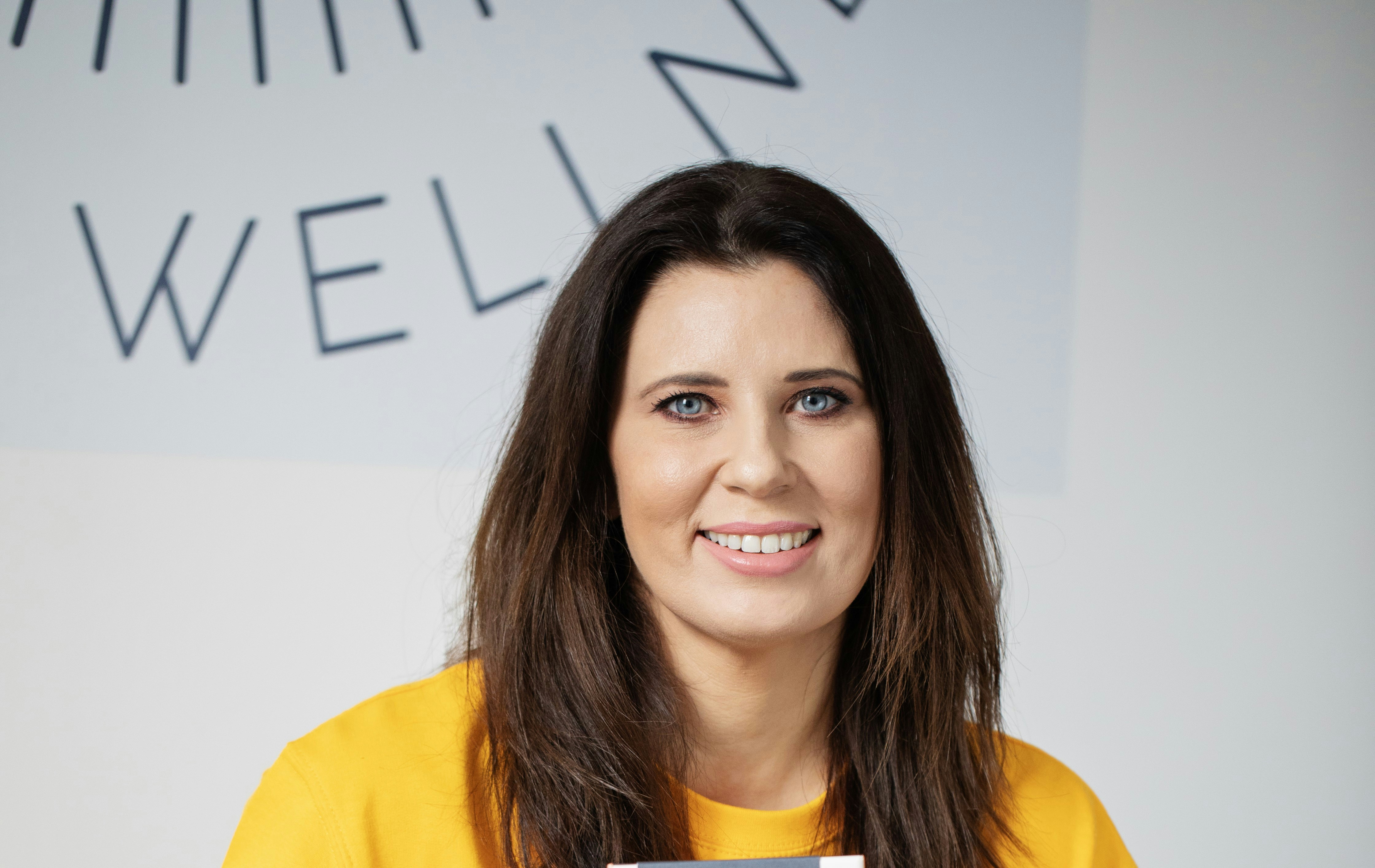 Woman with dark hair smiling, wearing yellow shirt.