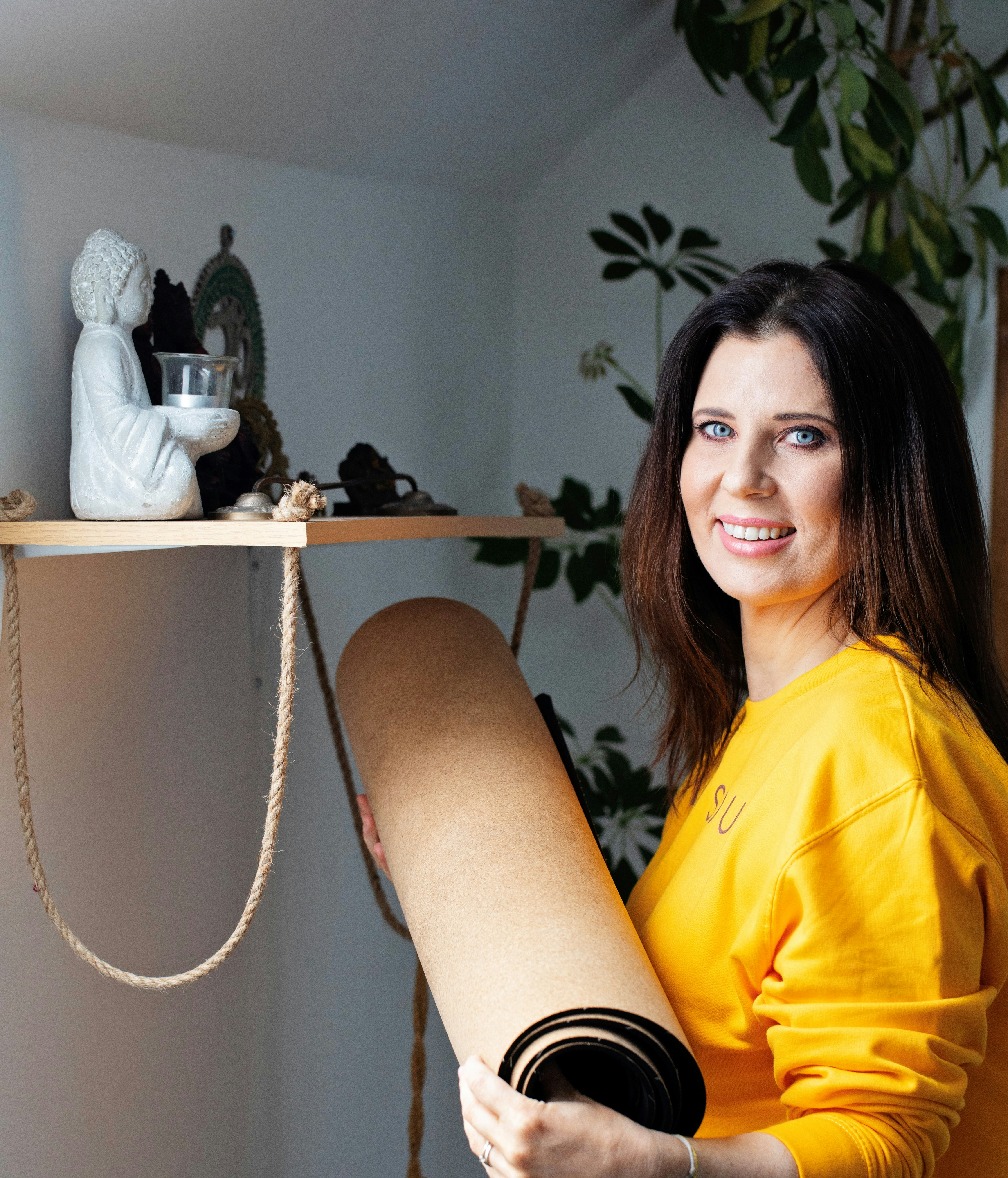 Mujer con jersey amarillo sosteniendo una esterilla de yoga