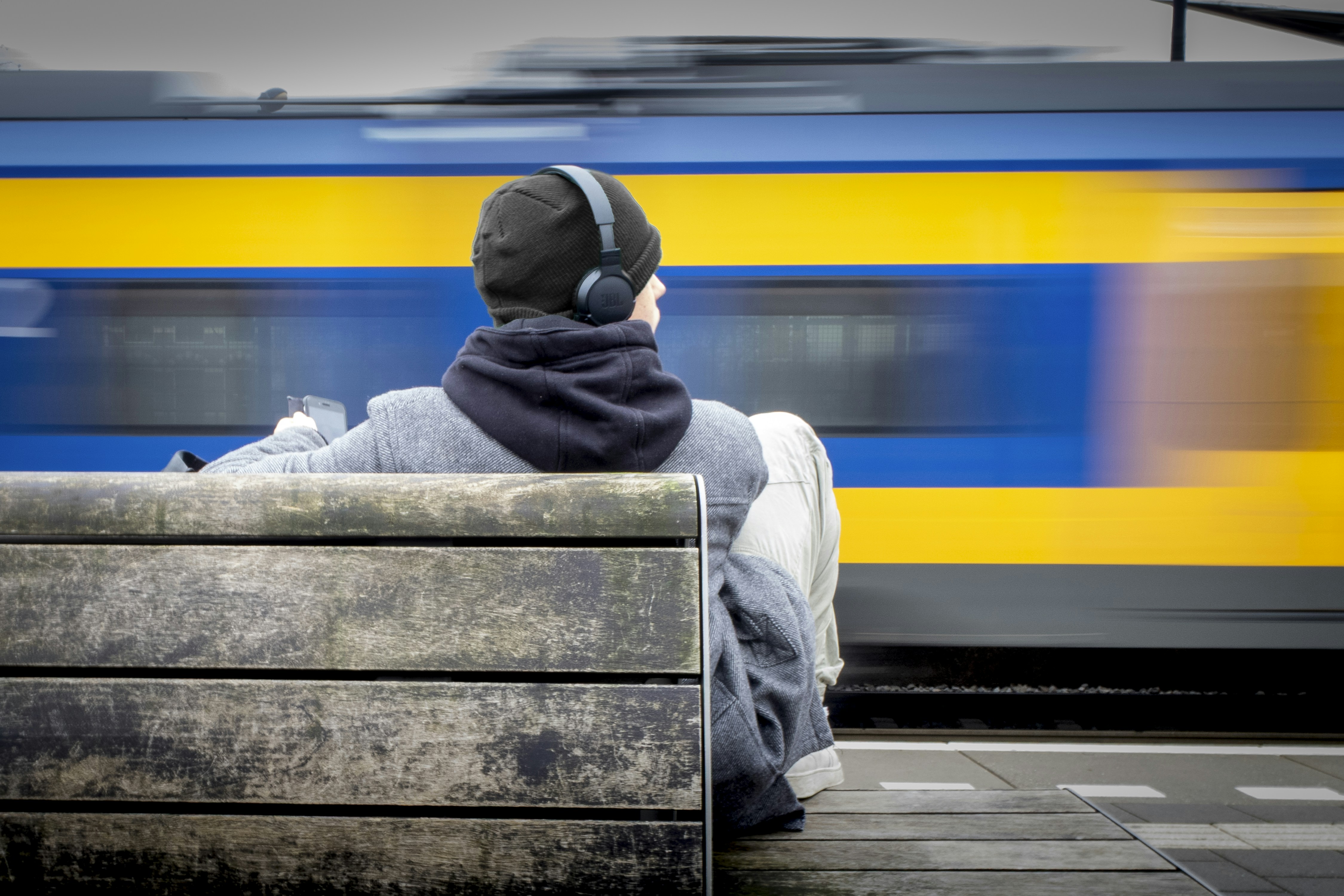 Person with headphones watches a blurred train pass by.