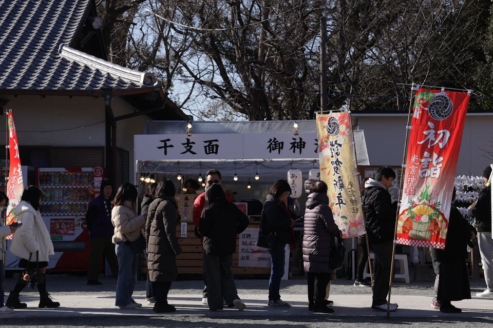 Visitors queueing at a traditional food stall with hanging banners at a Tokyo shrine during the Hatsumode New Year period