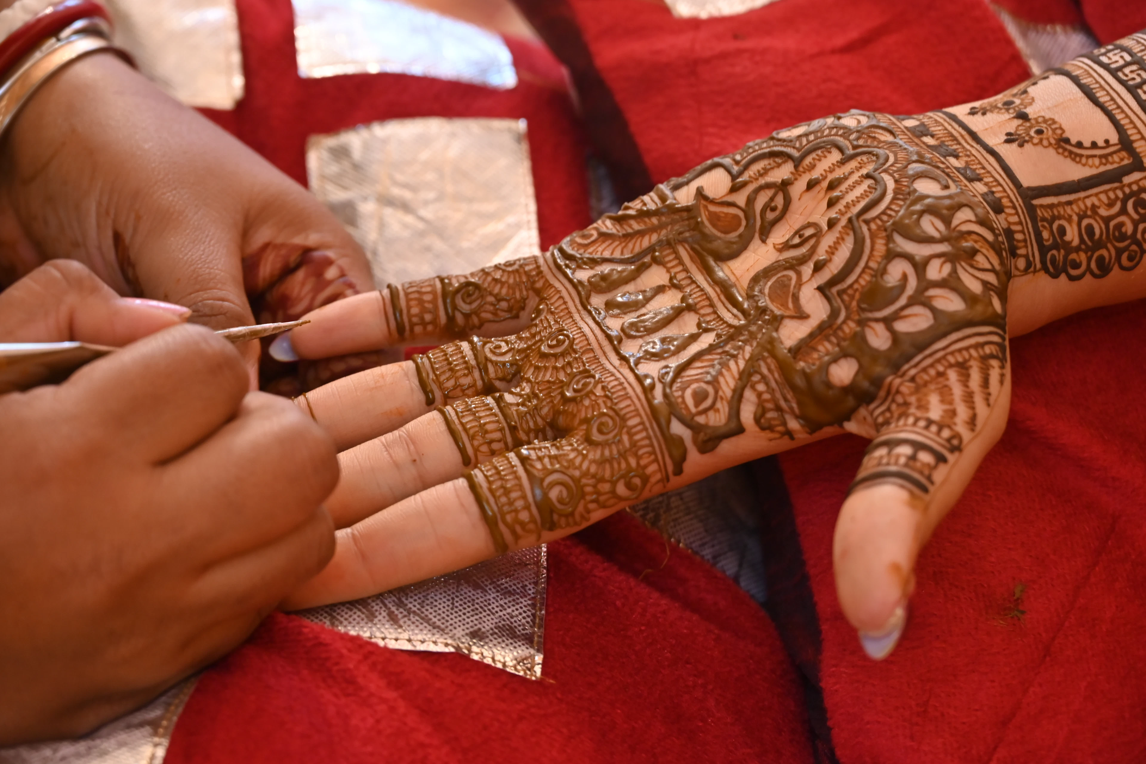 An artist finishing an intricate bridal mehendi design across a client's palm and fingers