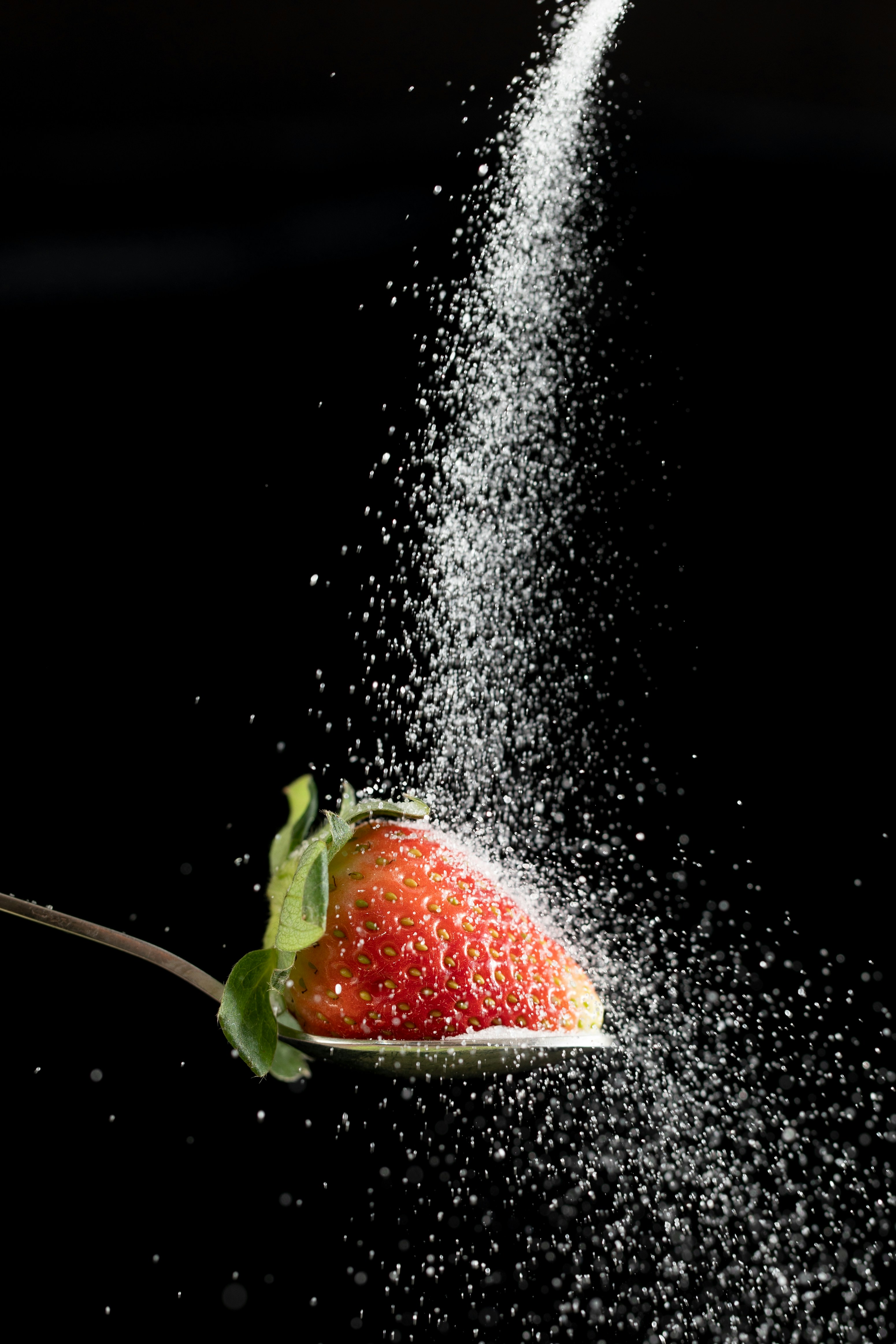 Sugar being poured onto a strawberry on a spoon.