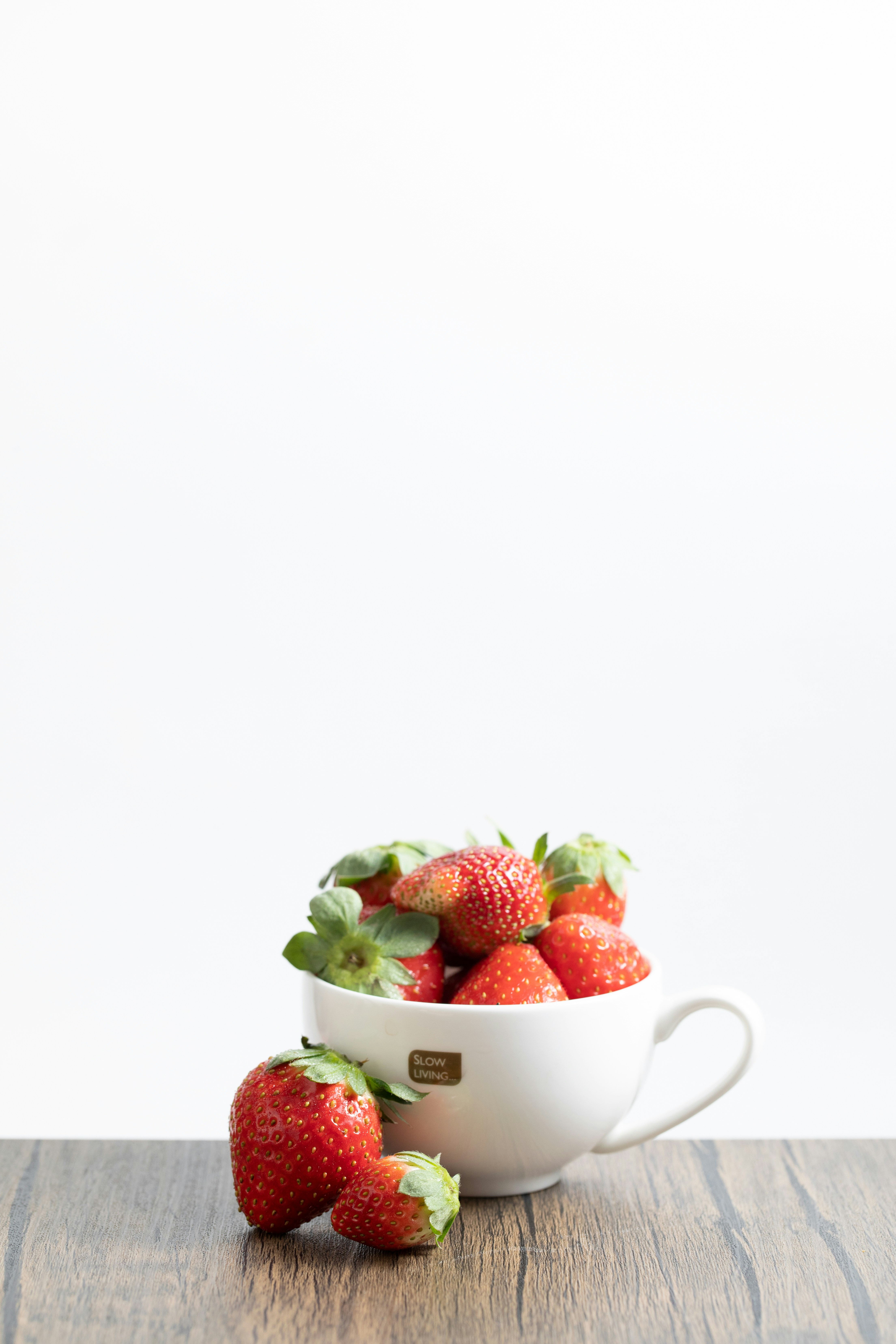 Fresh strawberries in a white cup on a wooden surface.