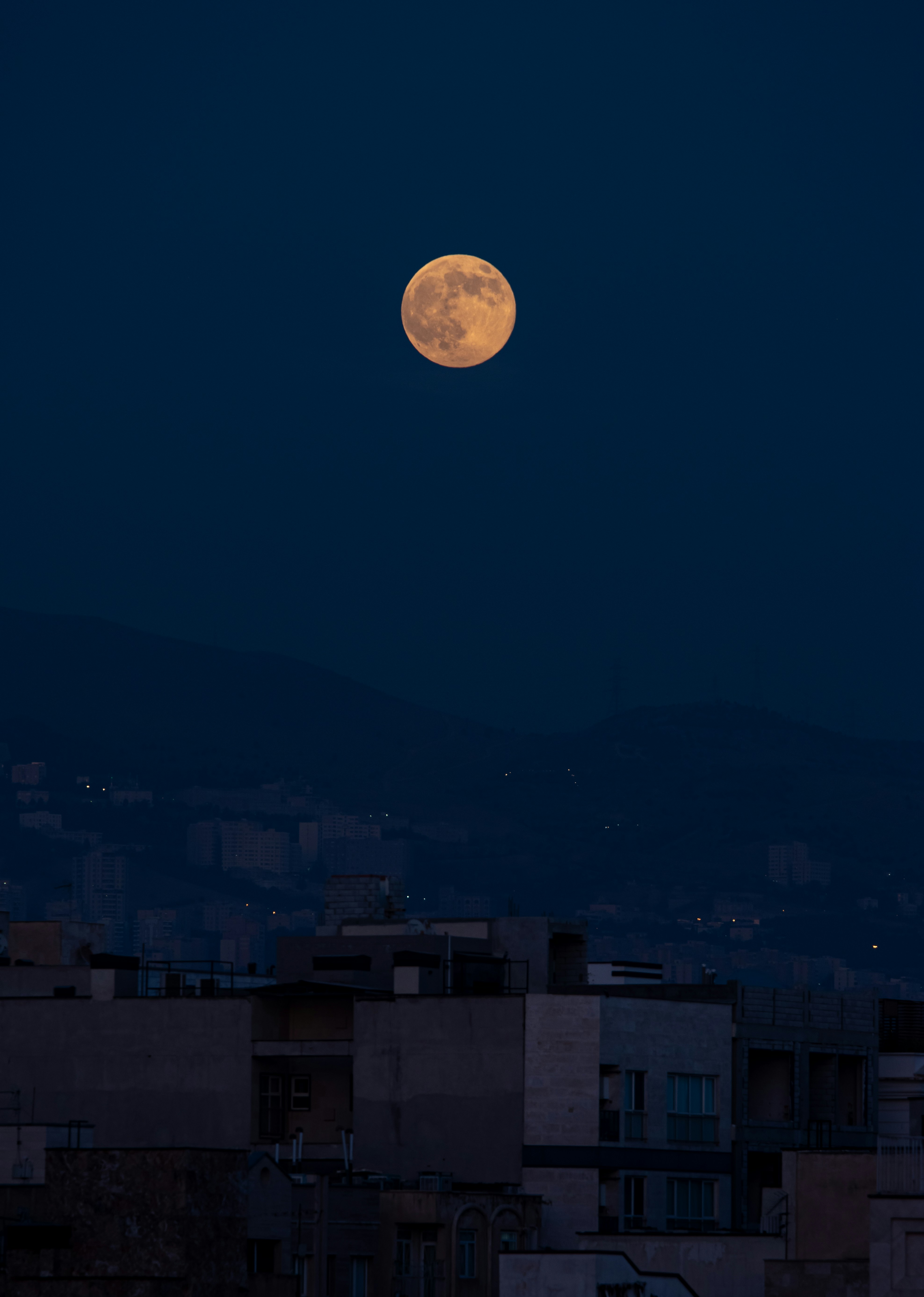 La luna llena se alza sobre el horizonte oscuro de una ciudad.