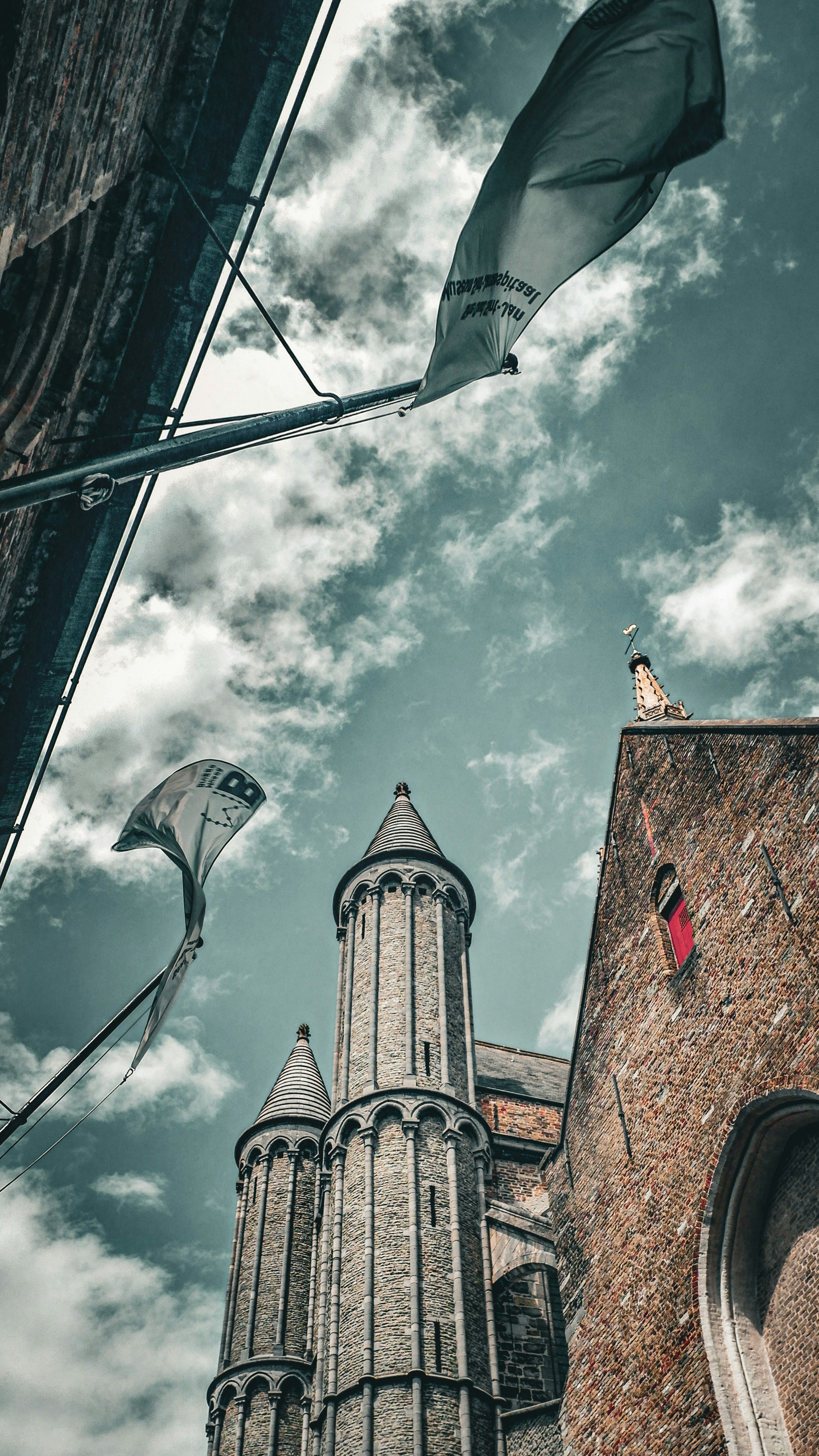 Two flags fly near a historic brick building and tower.
