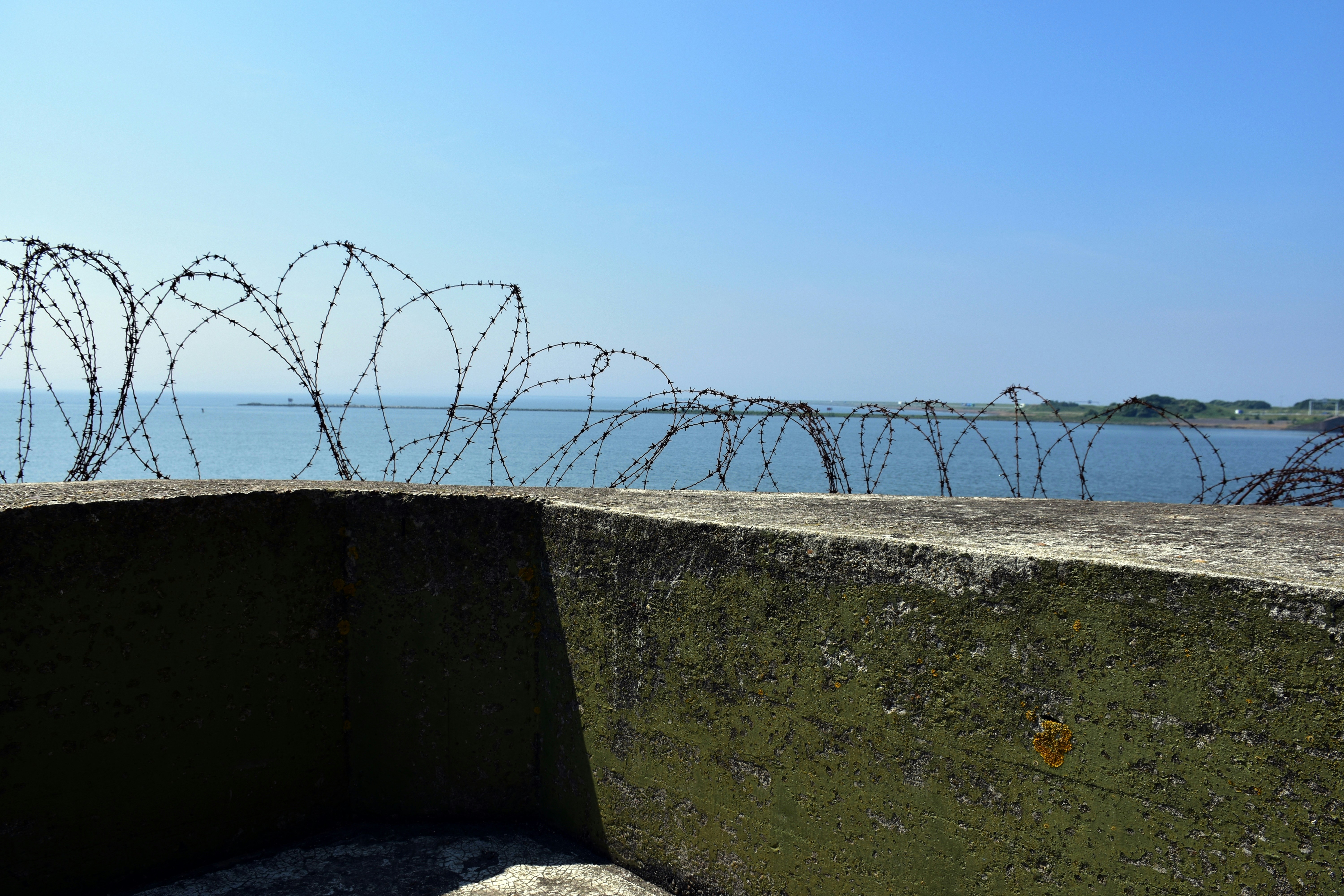 Barbed wire fence overlooking the ocean under a clear sky