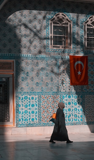 Woman in hijab walks past tiled wall with turkish flag.