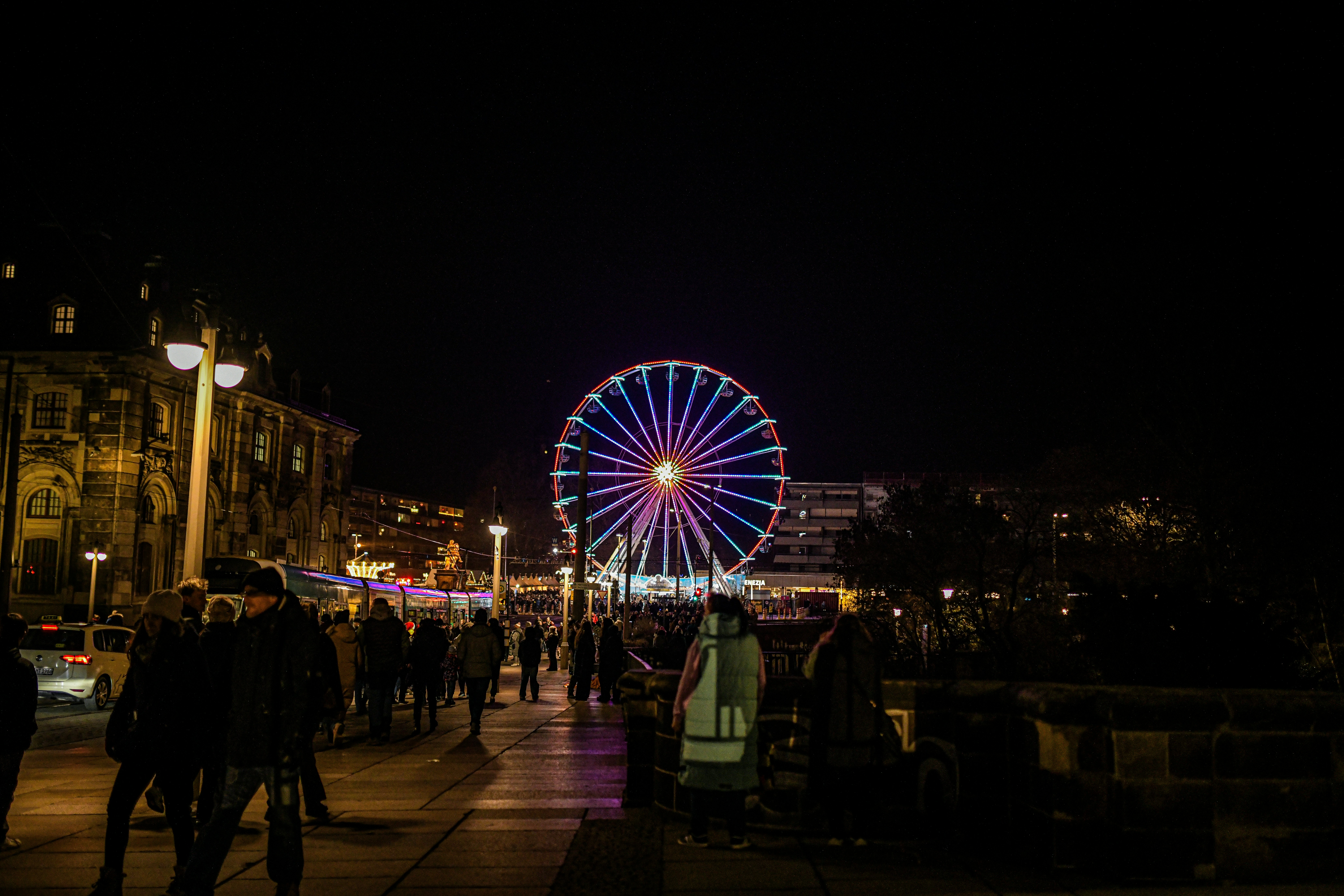 Ferris wheel illuminated at night with people walking