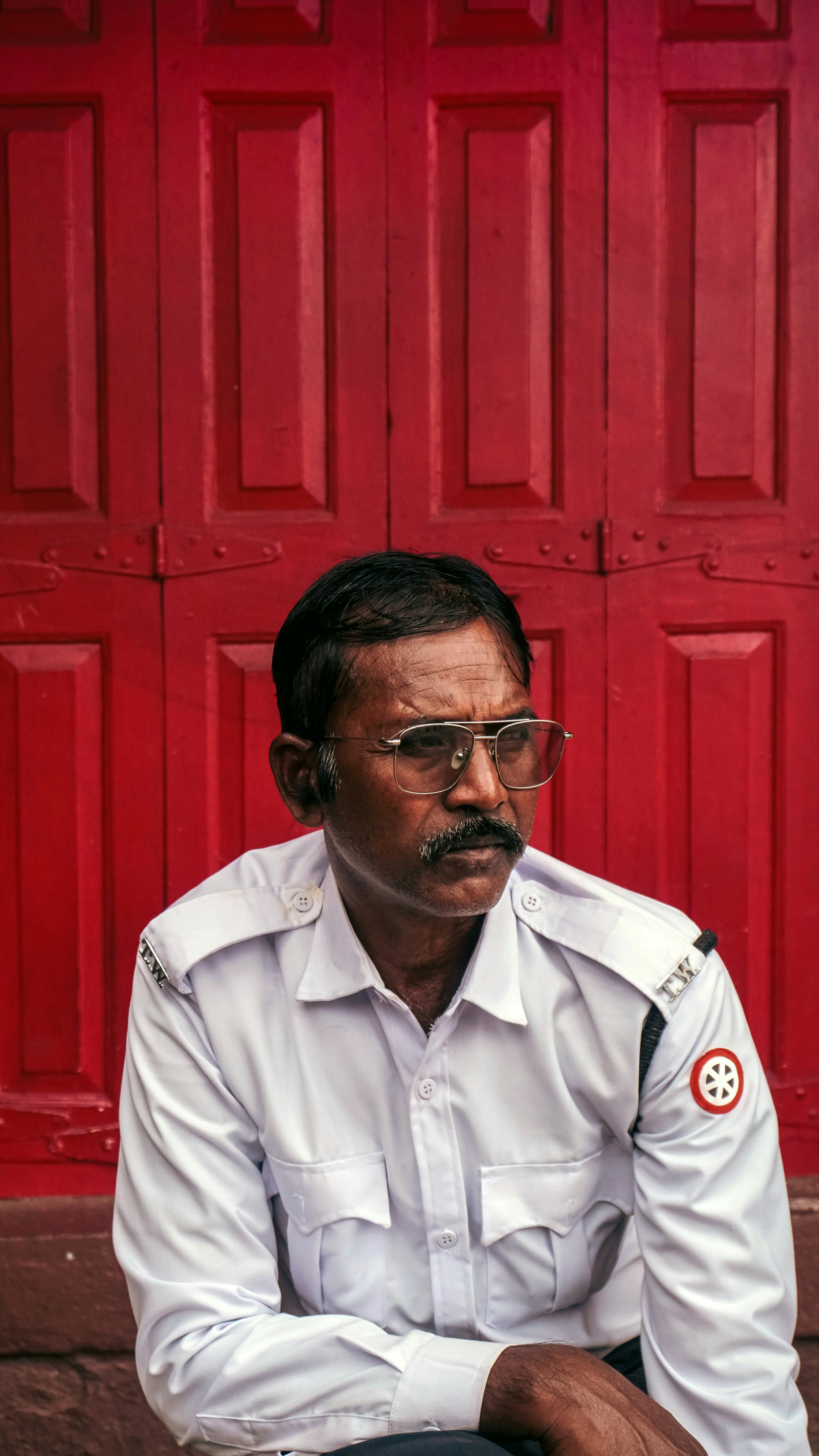 Man in uniform sits against red doors