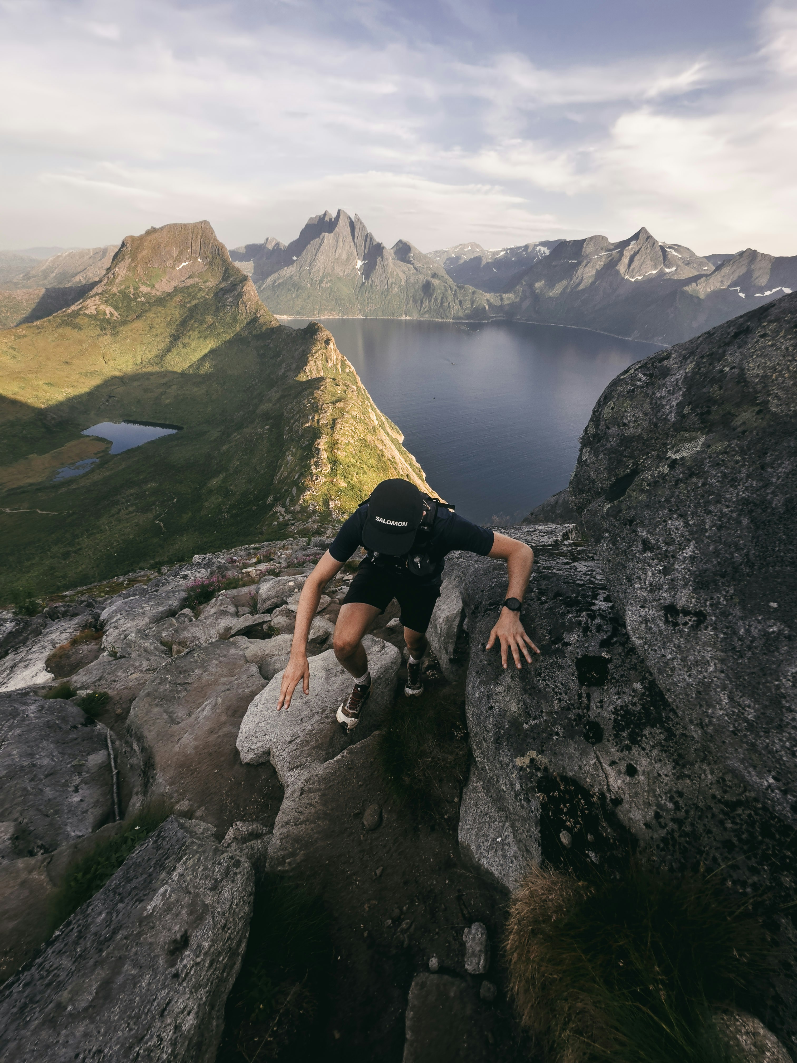 Man climbing a rocky mountain with a lake below.