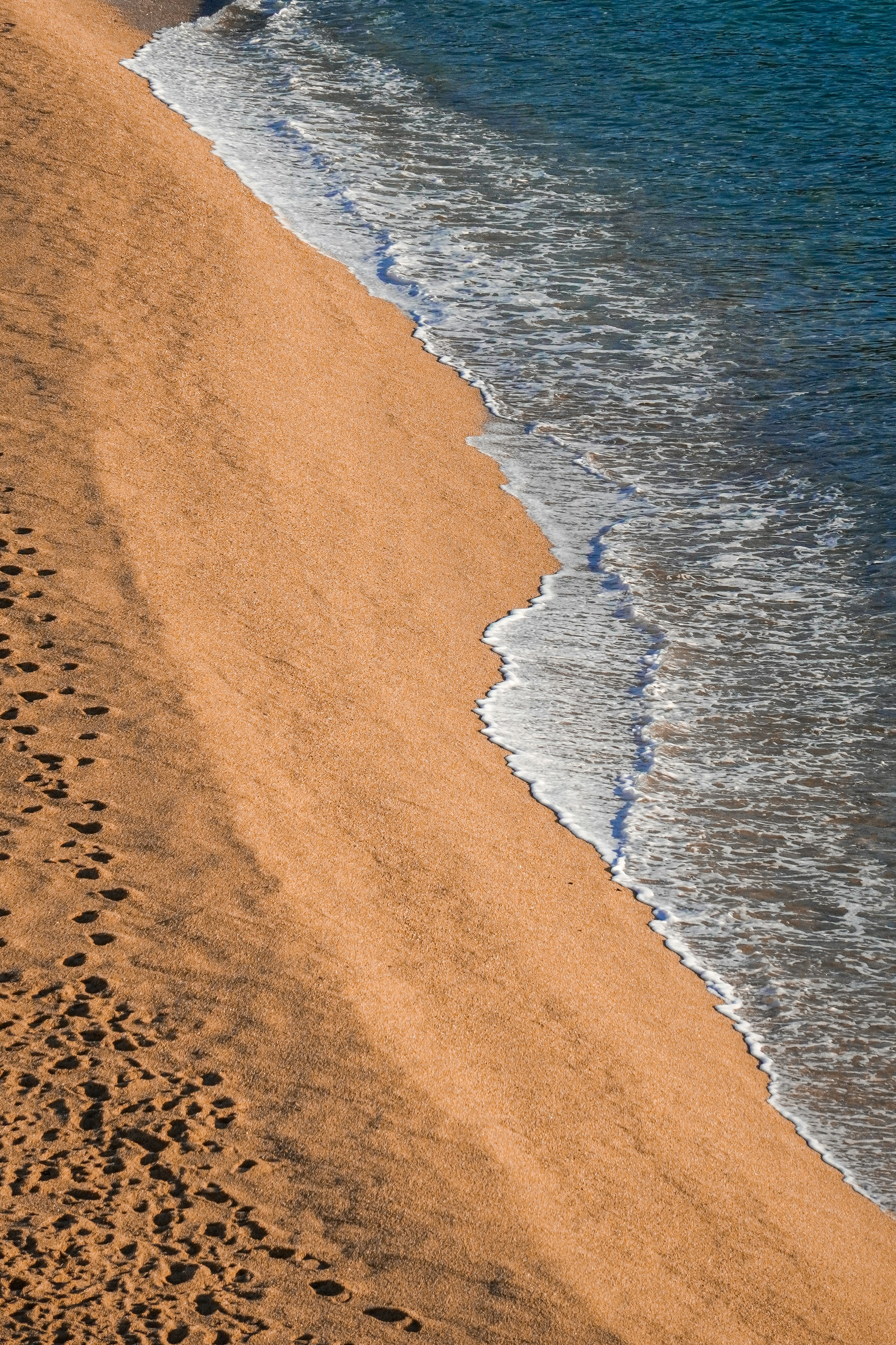 Footprints on a sandy beach with gentle ocean waves.