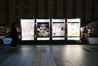 Four illuminated billboards in a city at night.