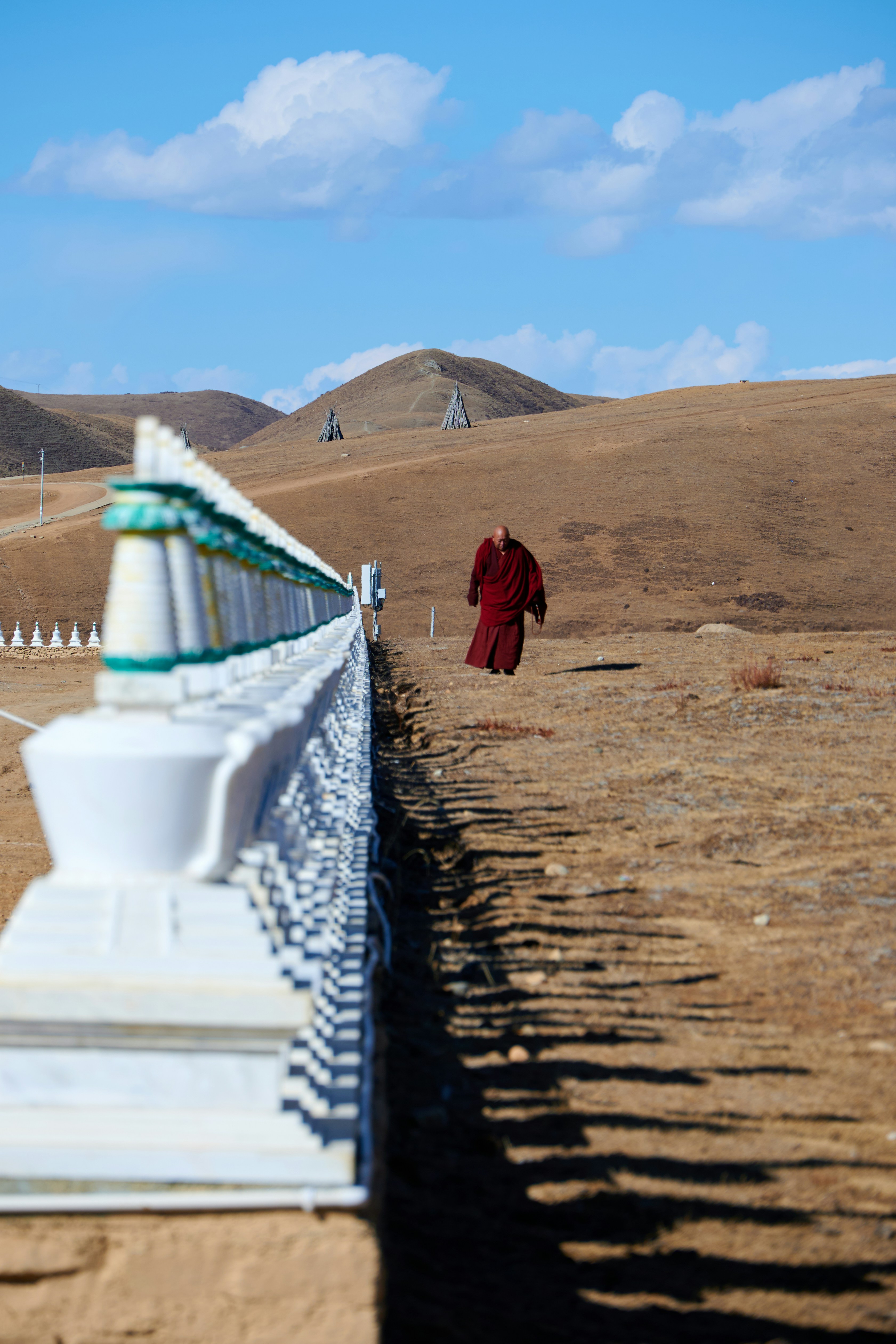 Monk in red robes walks on grassy hill.