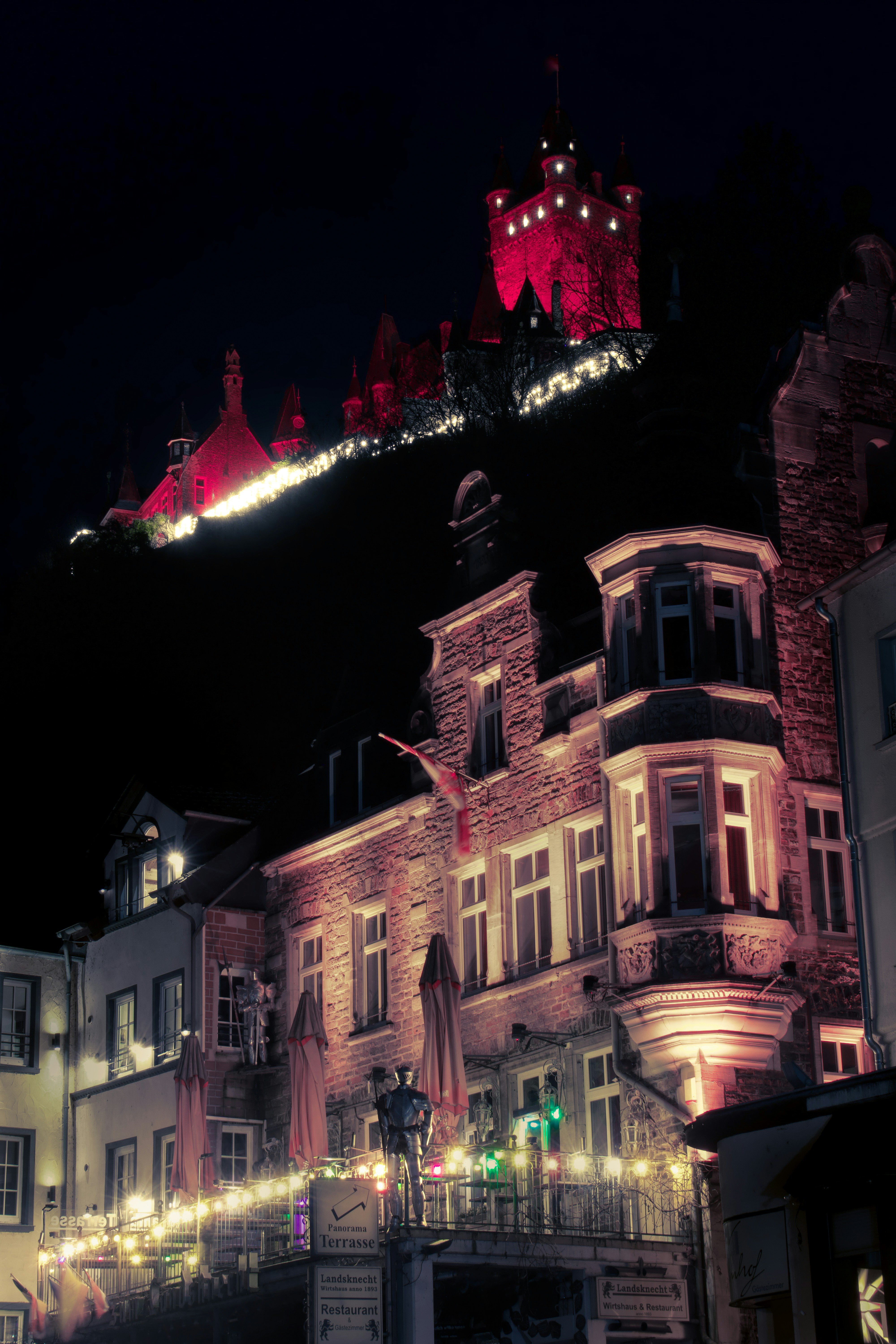 Castle illuminated in red light above town at night