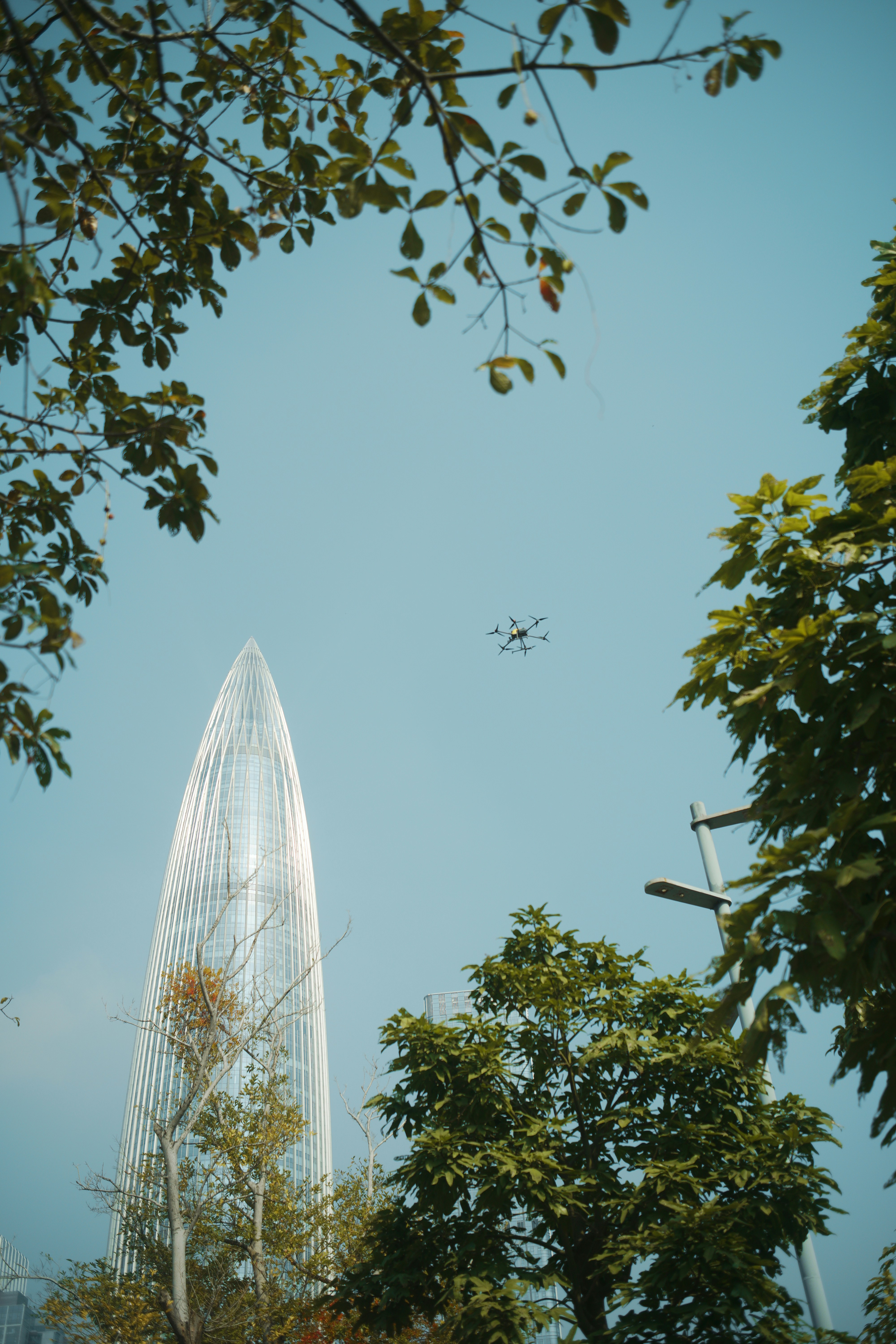 Modern skyscraper with trees and a drone flying.