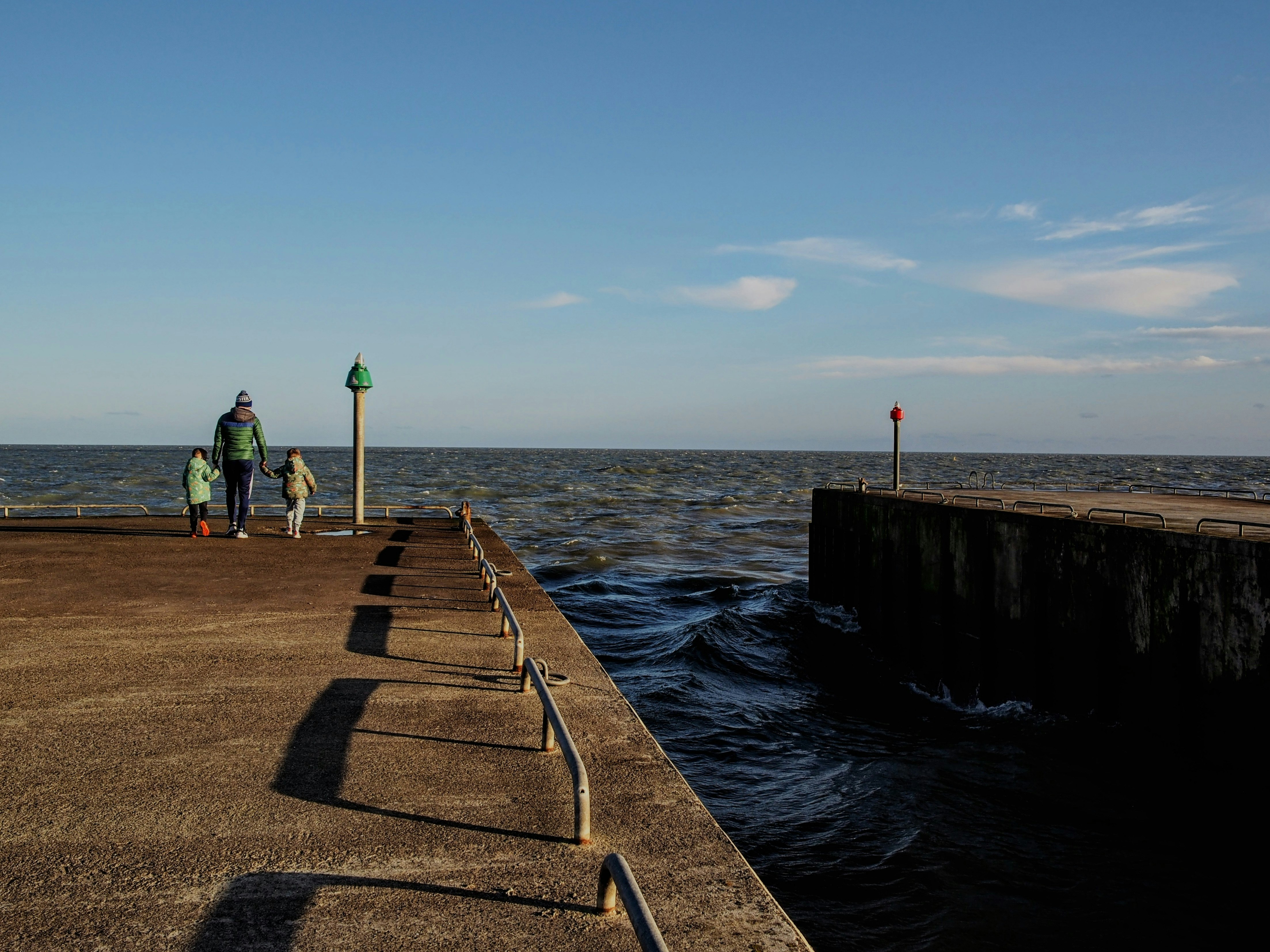 Two people walk on a pier by the ocean.