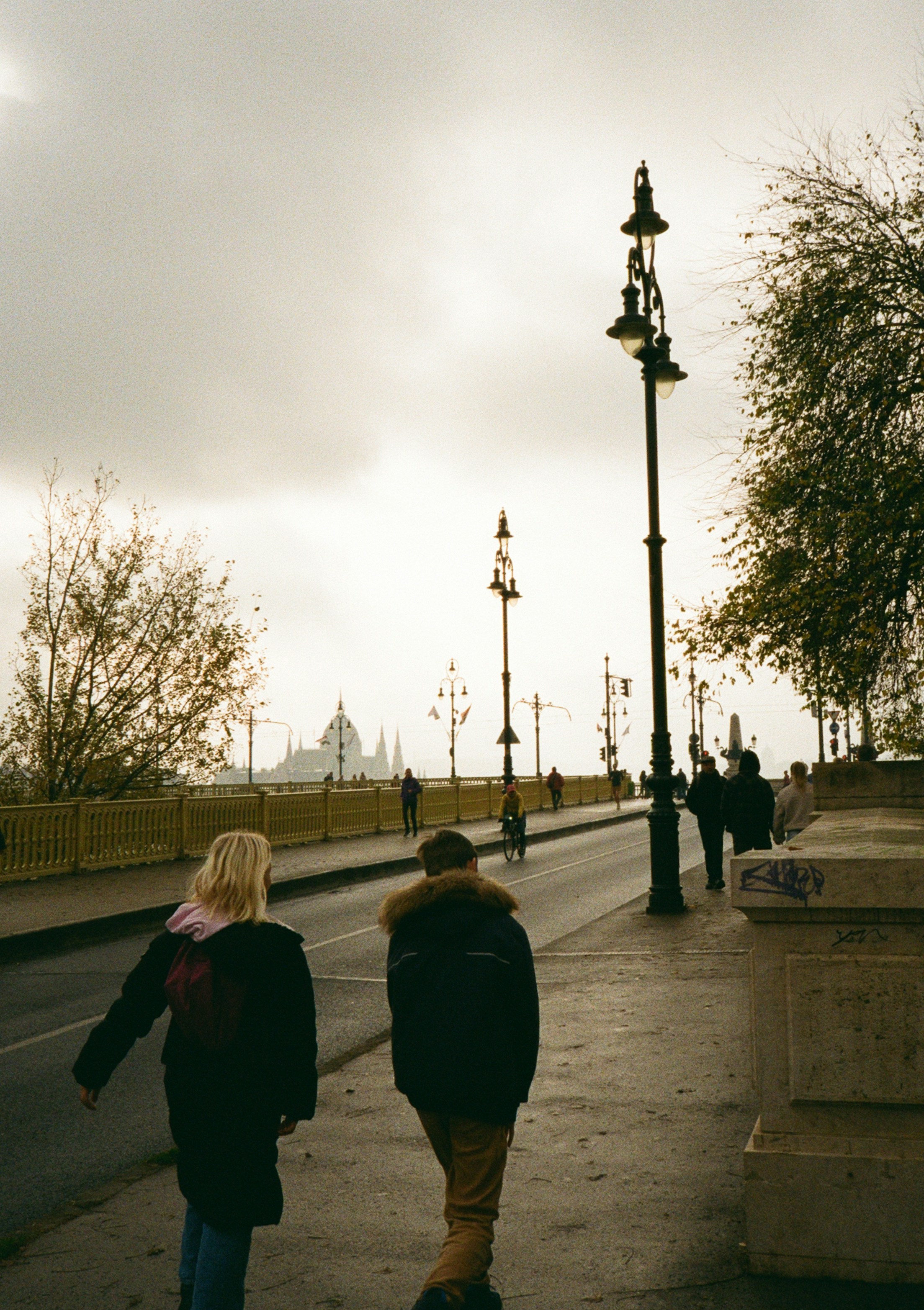 Two people walk on a bridge towards a domed building.