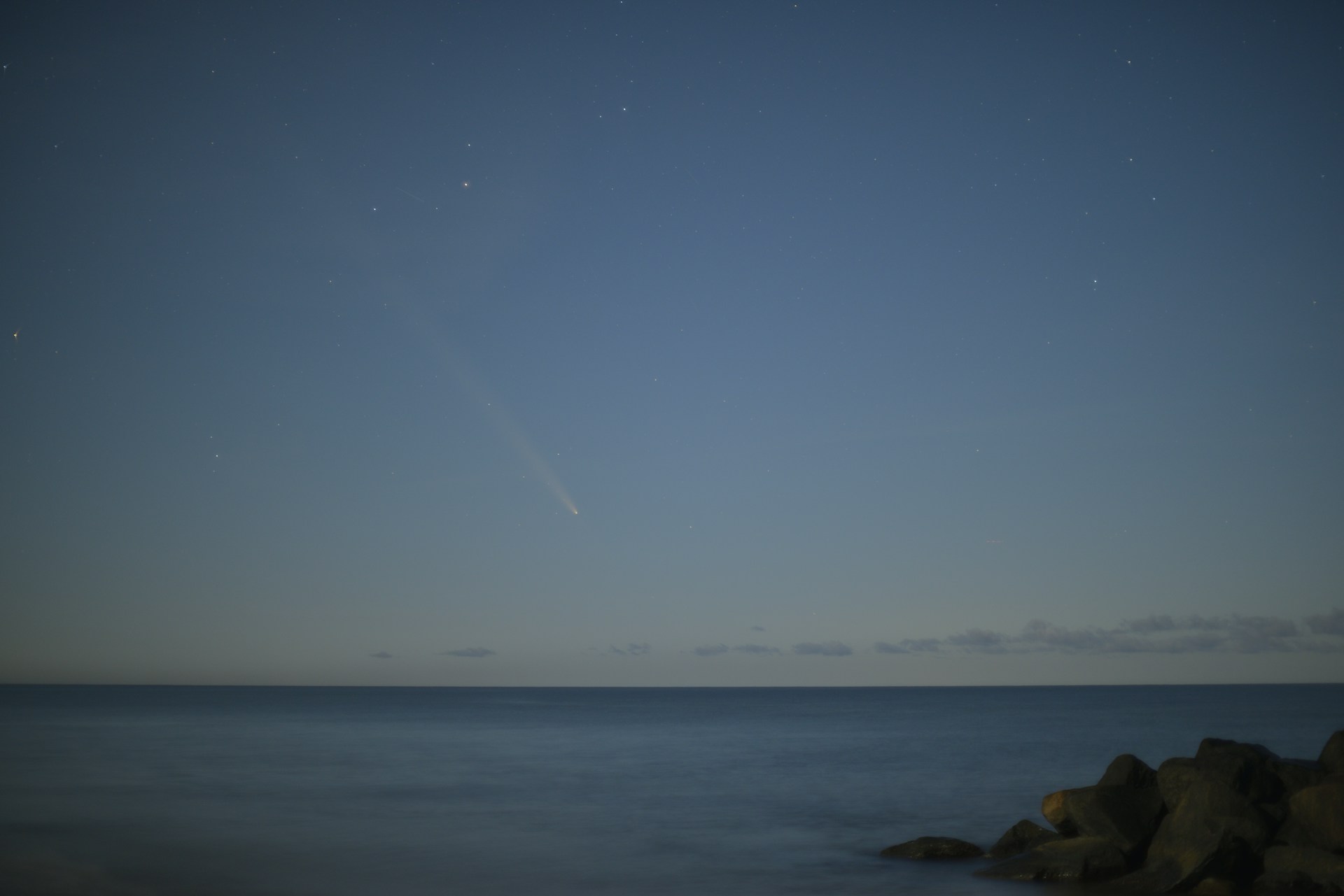 Comet streaking across the night sky over ocean