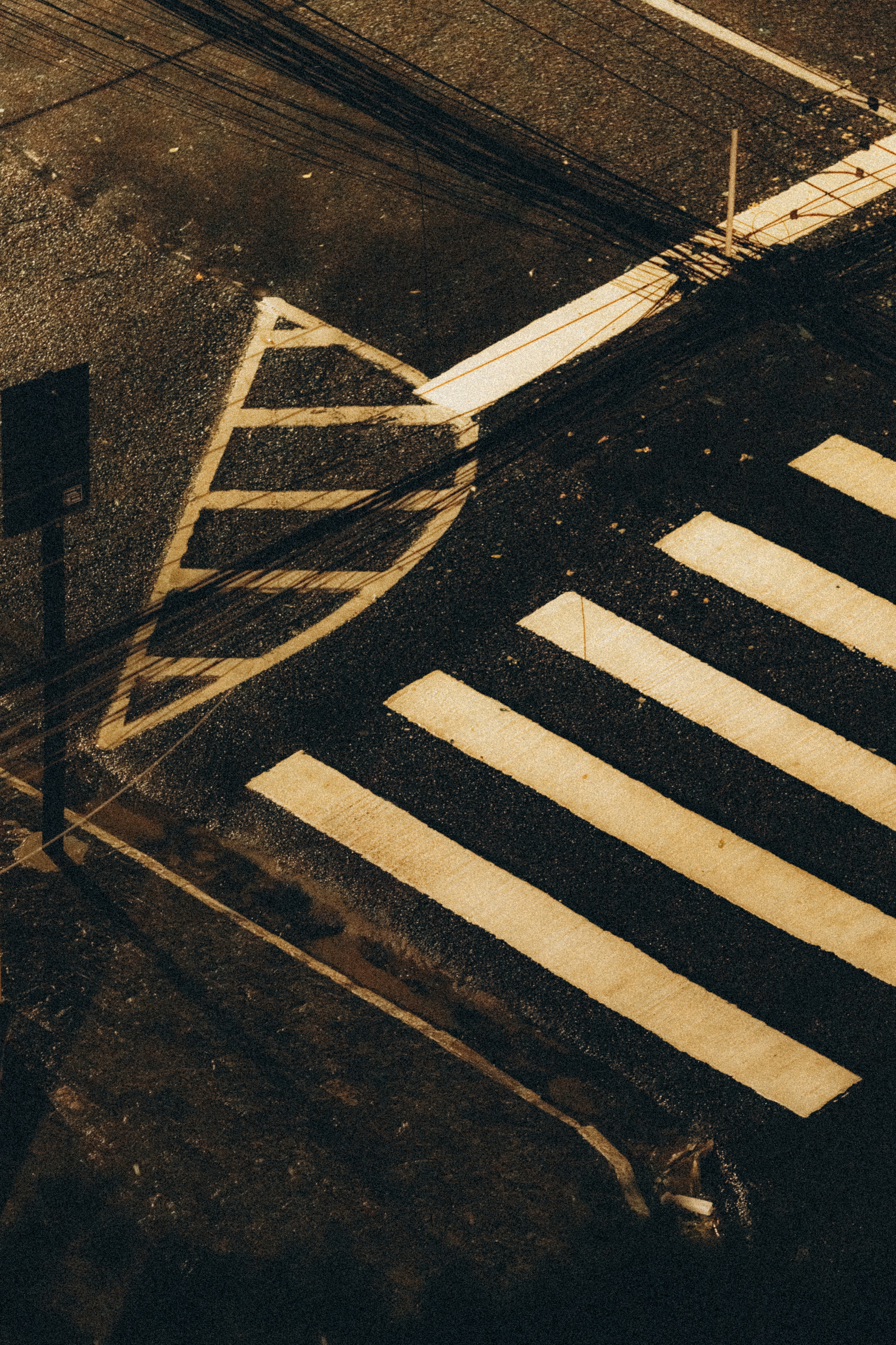 A wet crosswalk with yellow markings and overhead wires.