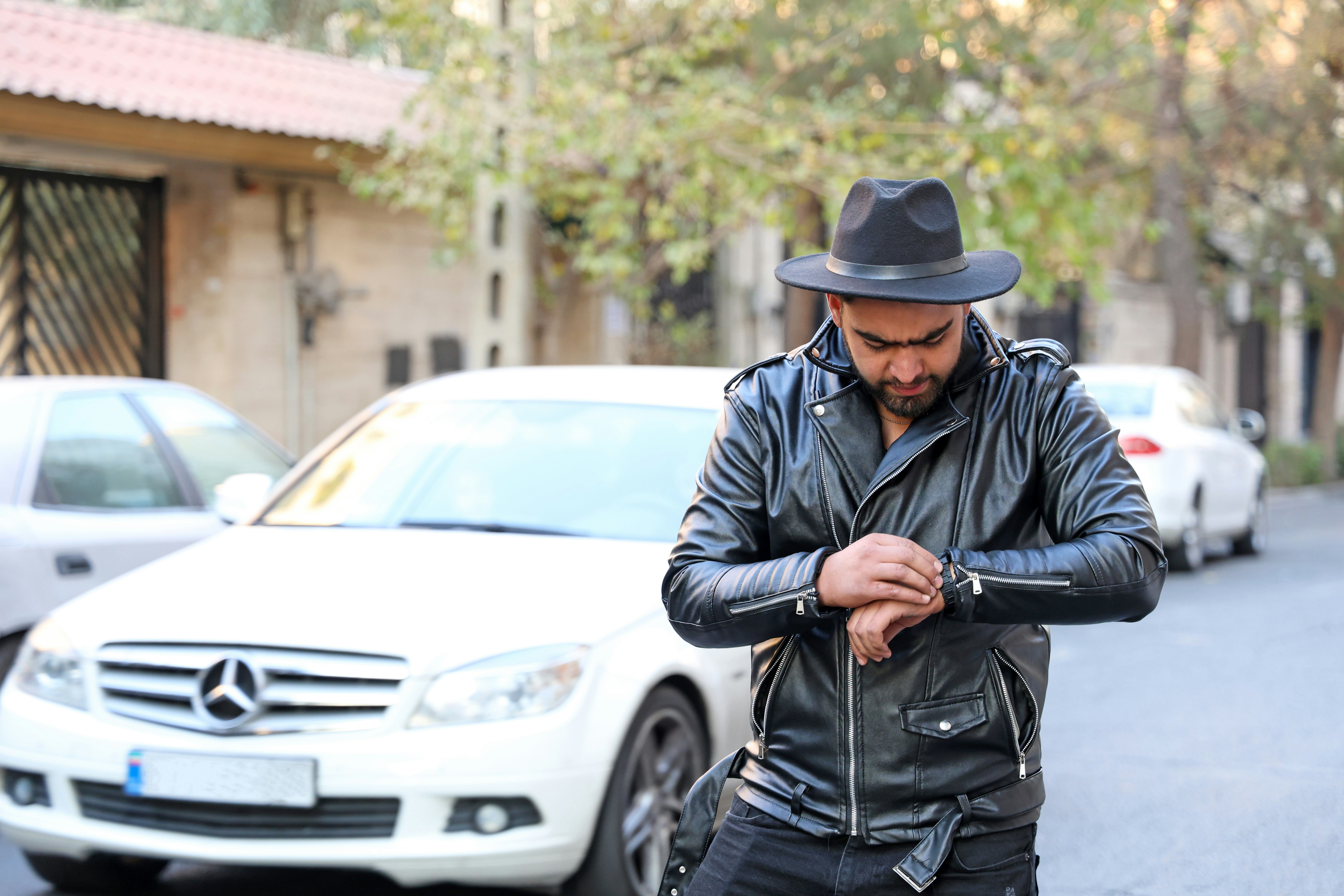 Man in black hat and leather jacket checks watch.
